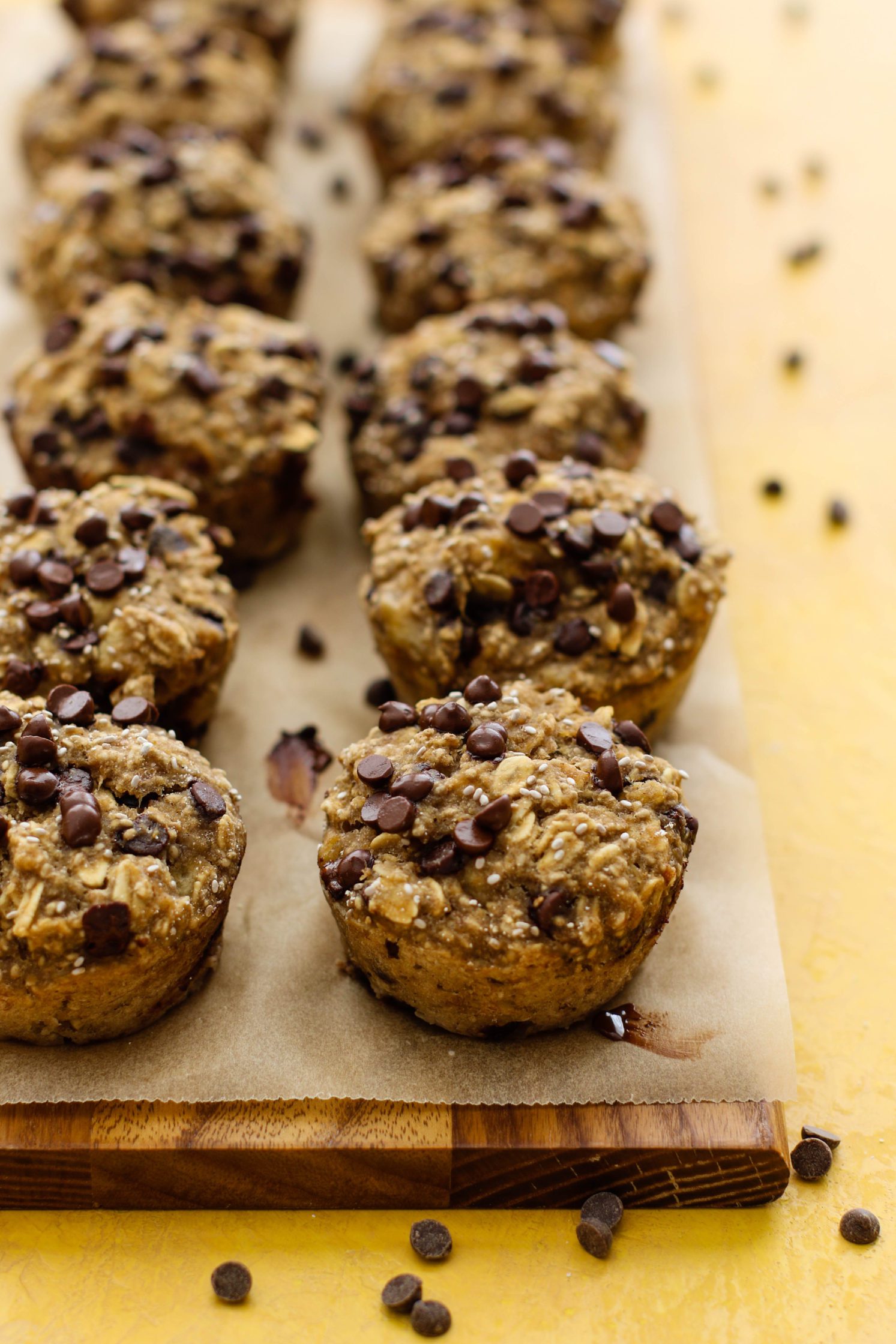 Banana Chia Chocolate Chip Muffins served on parchment lined wooden board with chocolate chips scattered