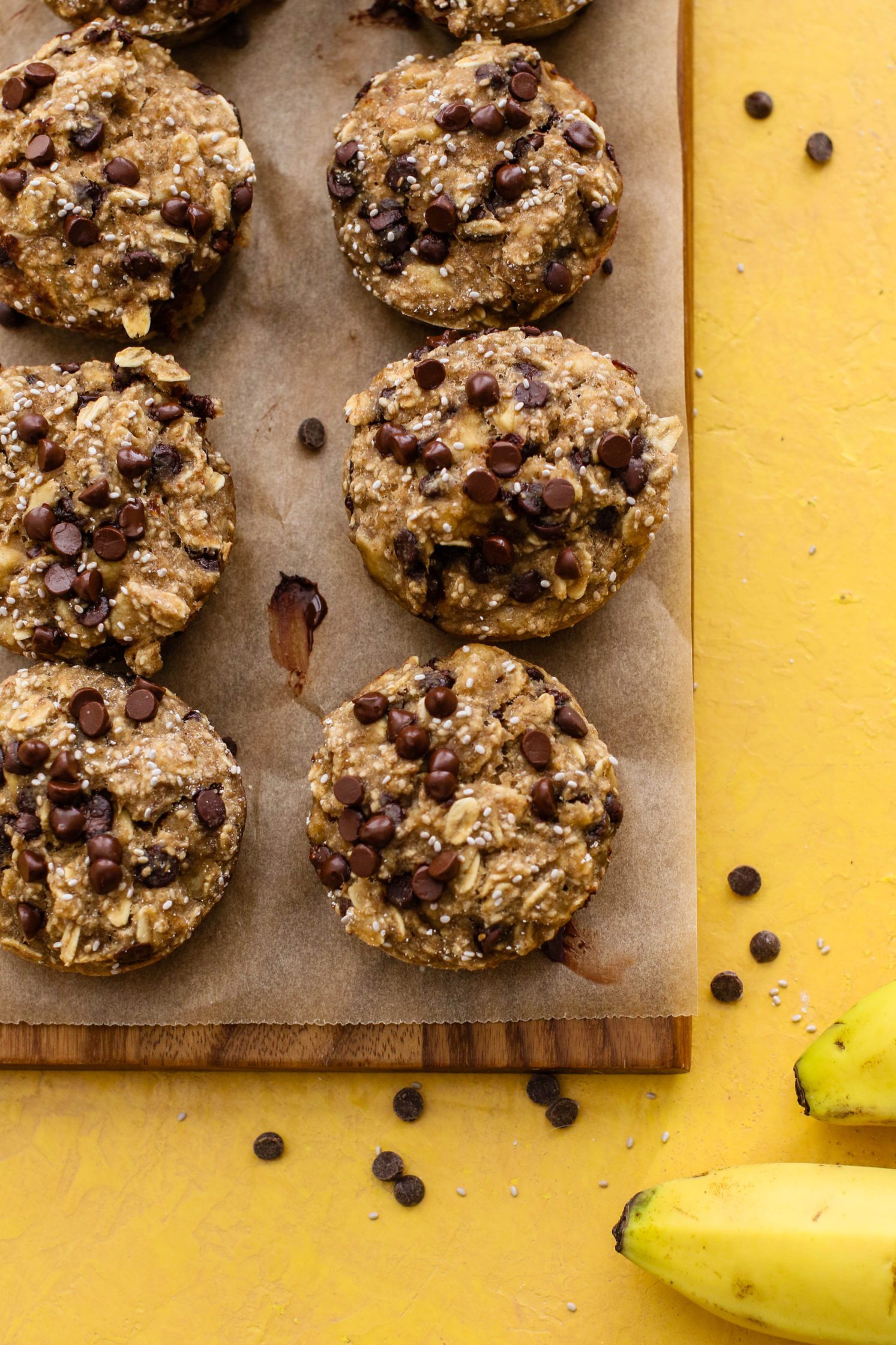 Banana Chia Chocolate Chip Muffins served on parchment lined wooden board with chocolate chips scattered