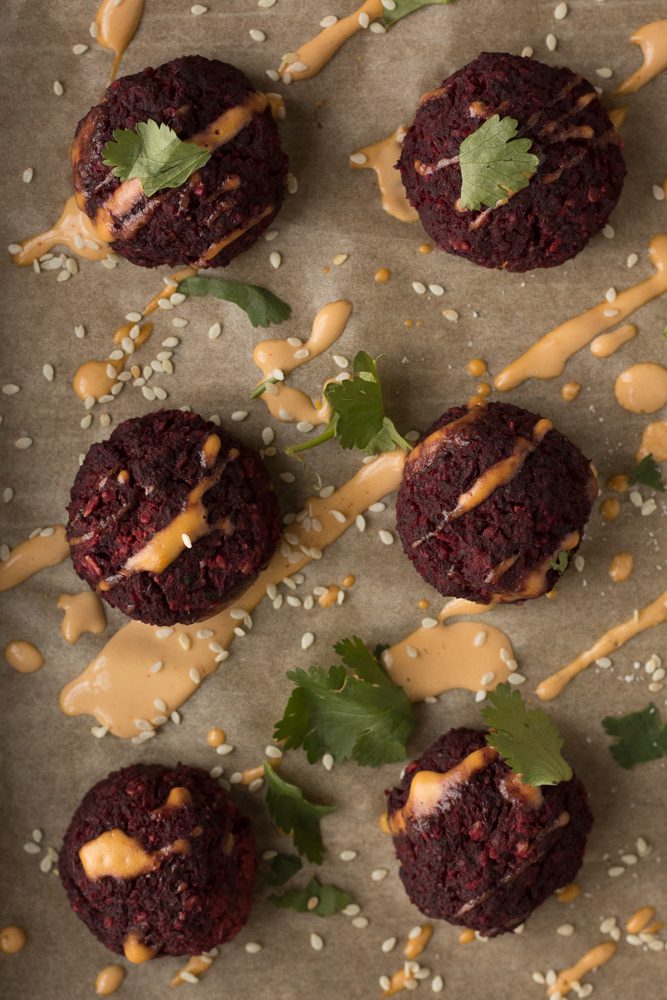 Lentil Walnut Beet Balls on parchment paper with Spicy Tahini Dressing drizzled by Flora & Vino