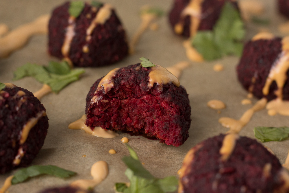 Lentil Walnut Beet Balls drizzled with Spicy Tahini Dressing with bite out of one by Flora & Vino