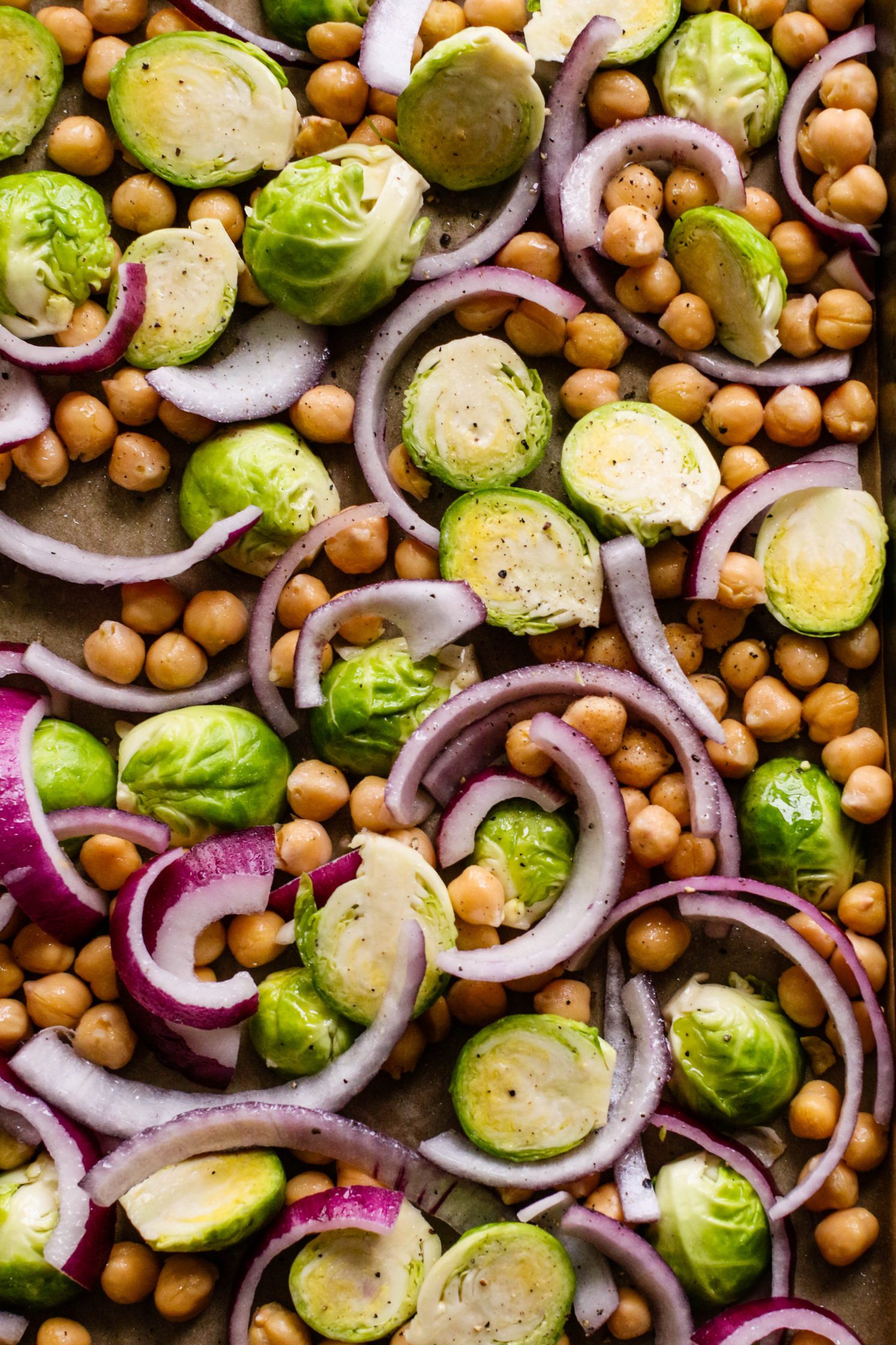 brussels sprouts, chickpeas, and red onion on parchment lined baking sheet by Flora & Vino