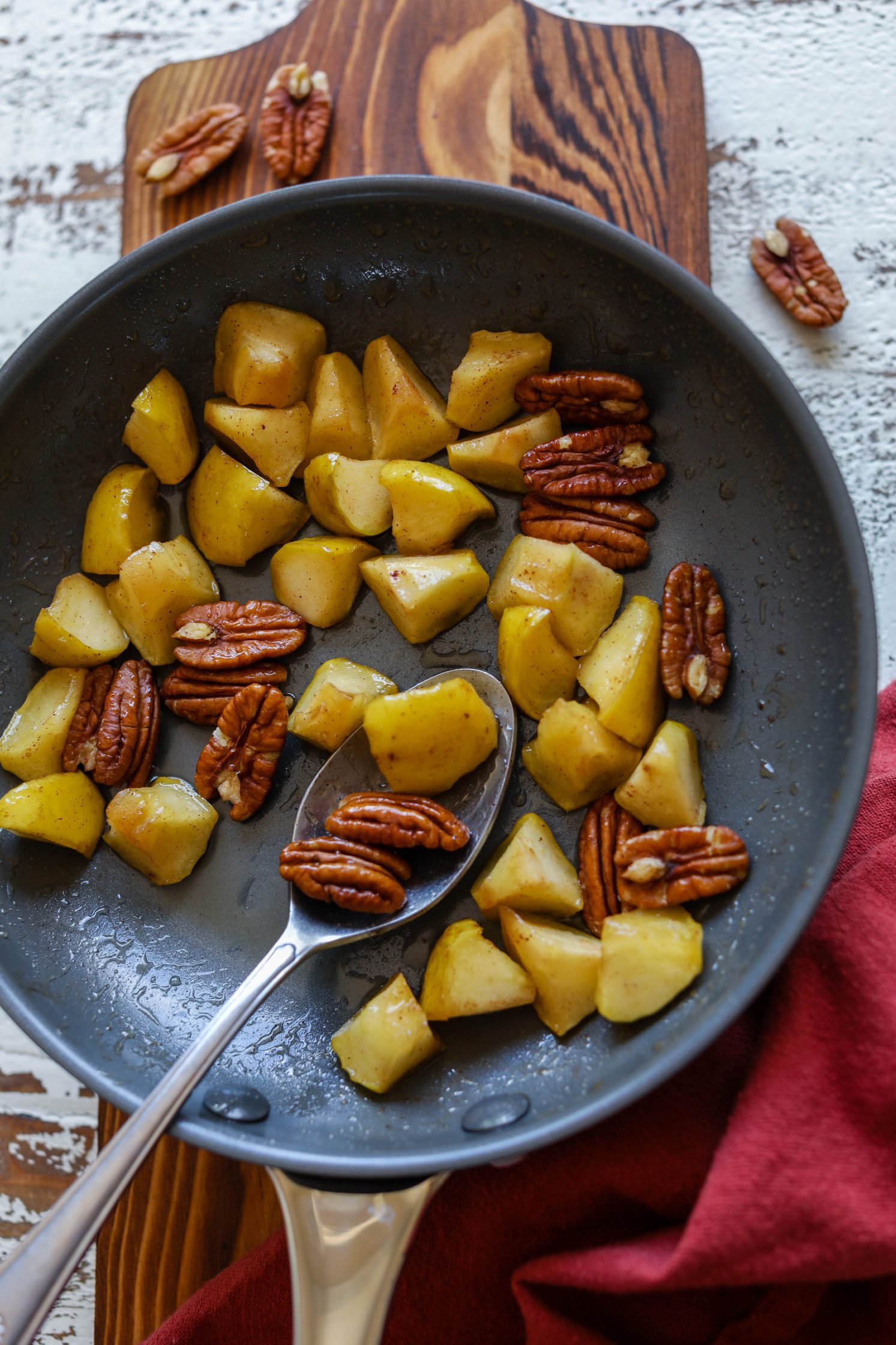 Sautéed Apples with pecans in a pan with a spoon by Flora & Vino 