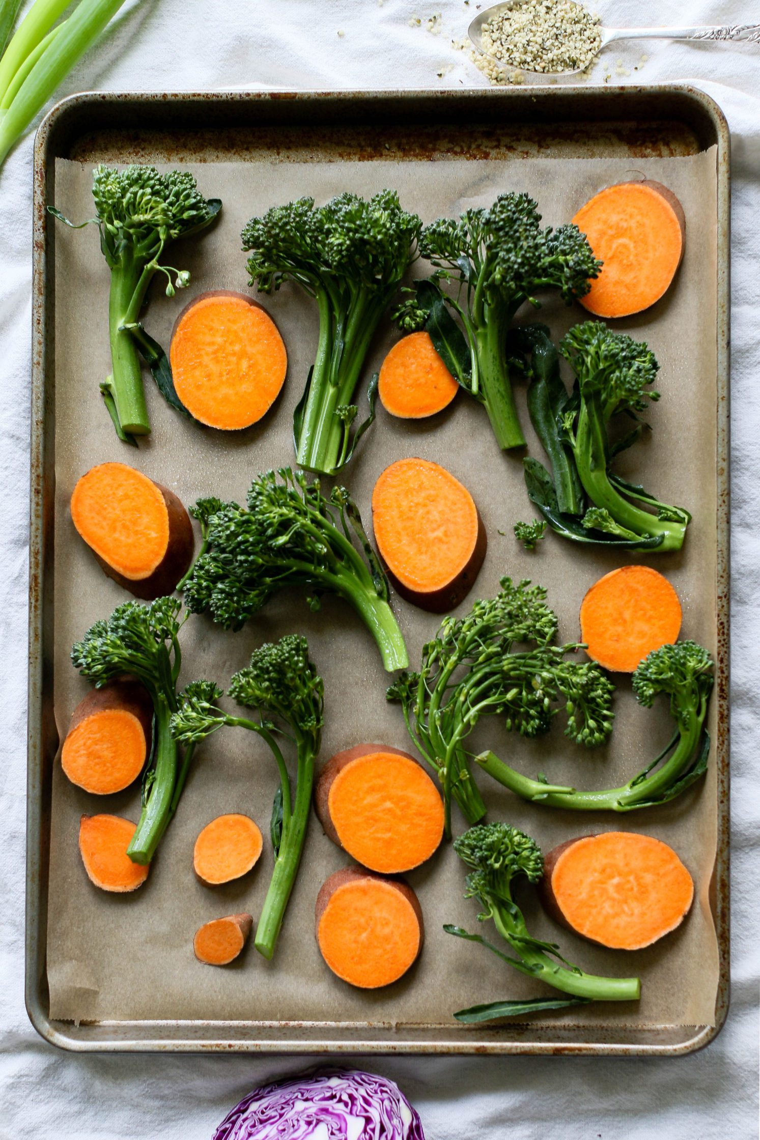 broccolini and sweet potato on parchment lined baking sheet