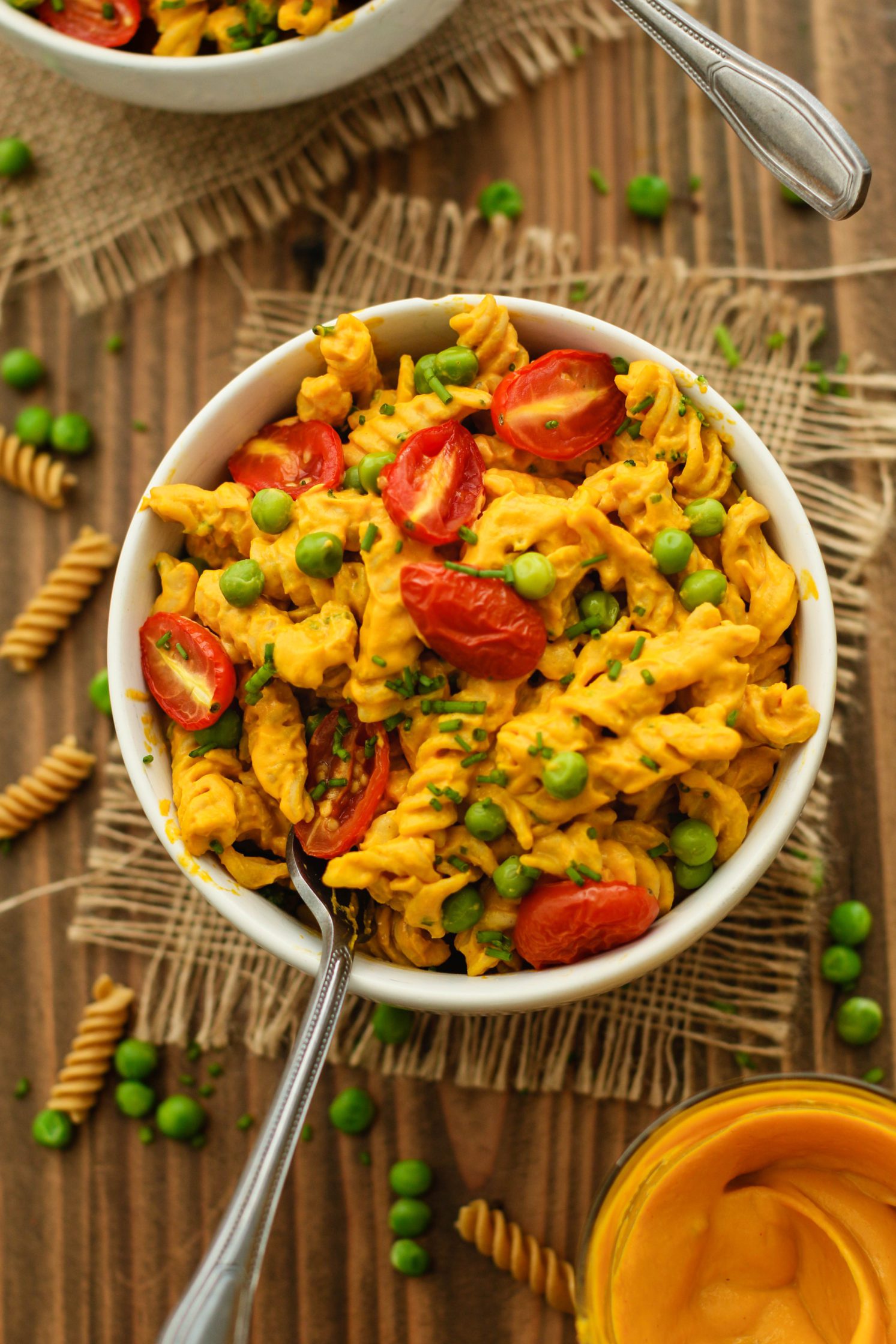 Mac 'N' Peas Bowls served in bowls with spoons on burlap squares on wooden board with dried pasta and peas scattered