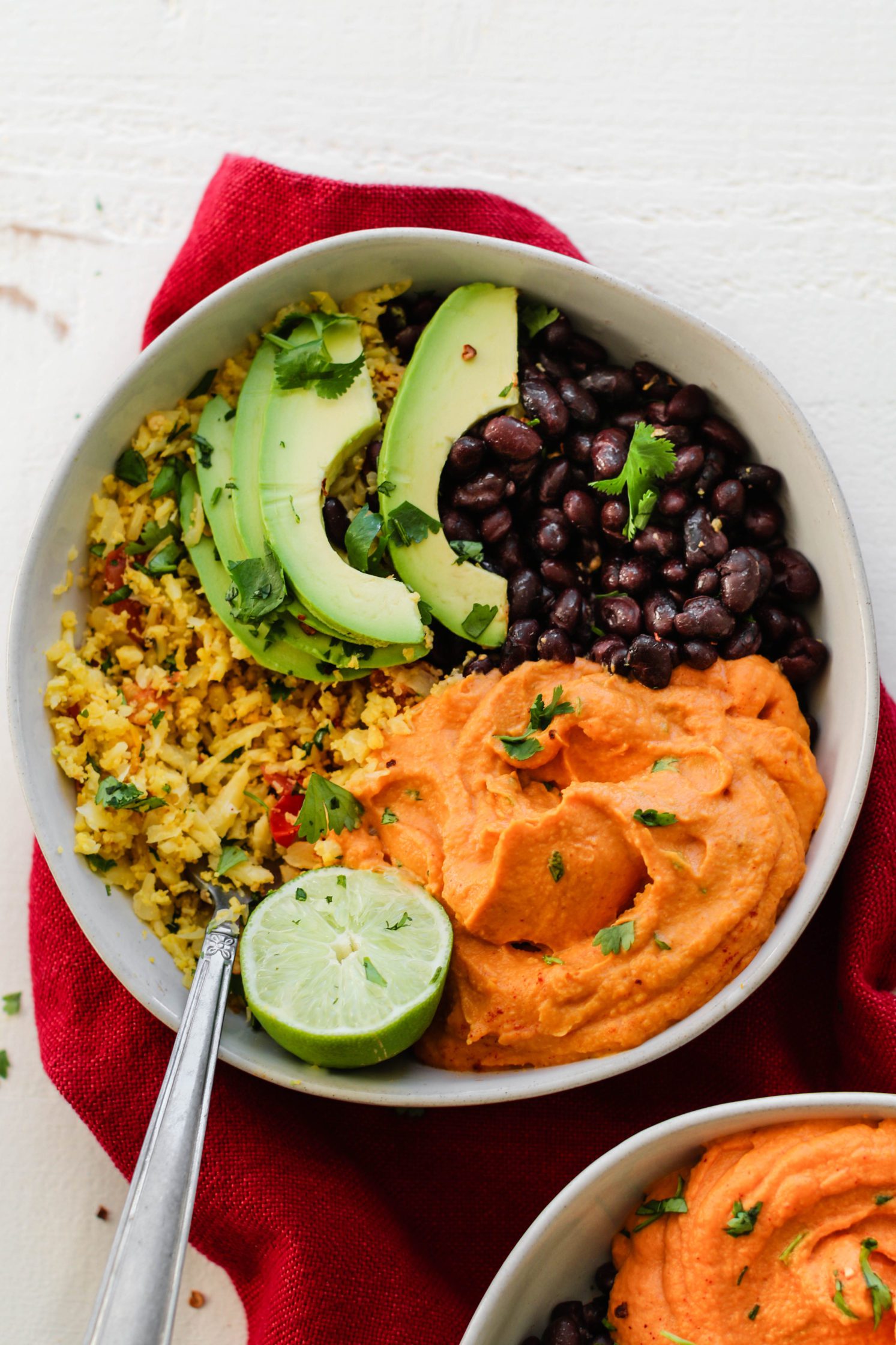 Smashed Burrito Bowls served in bowl with fork and red towel with avocado and lime