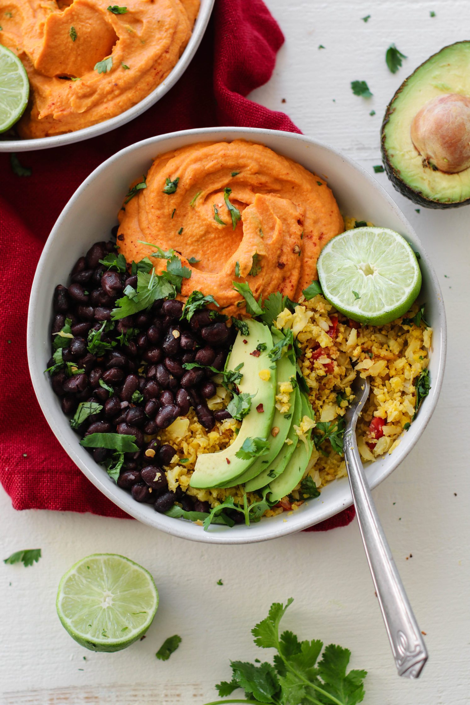 Smashed Burrito Bowls served in bowl with fork and red towel with avocado and lime