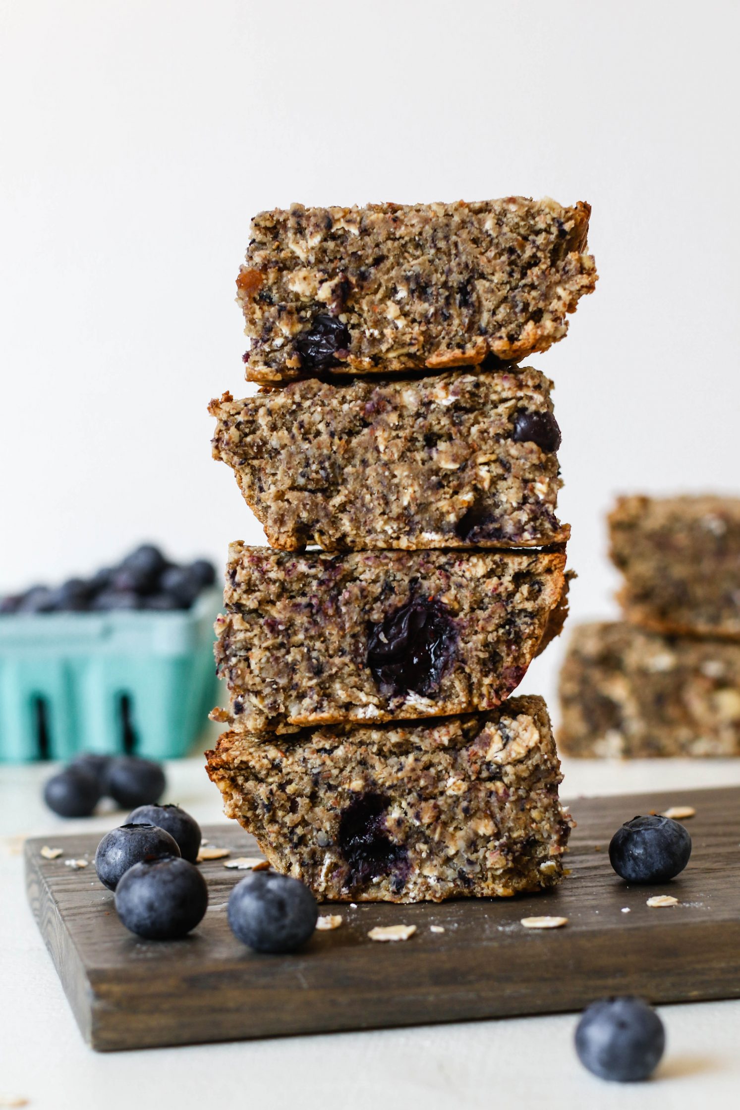 Blueberry Maple Baked Breakfast Bars stacked on wooden board surrounded by blueberries by Flora & Vino