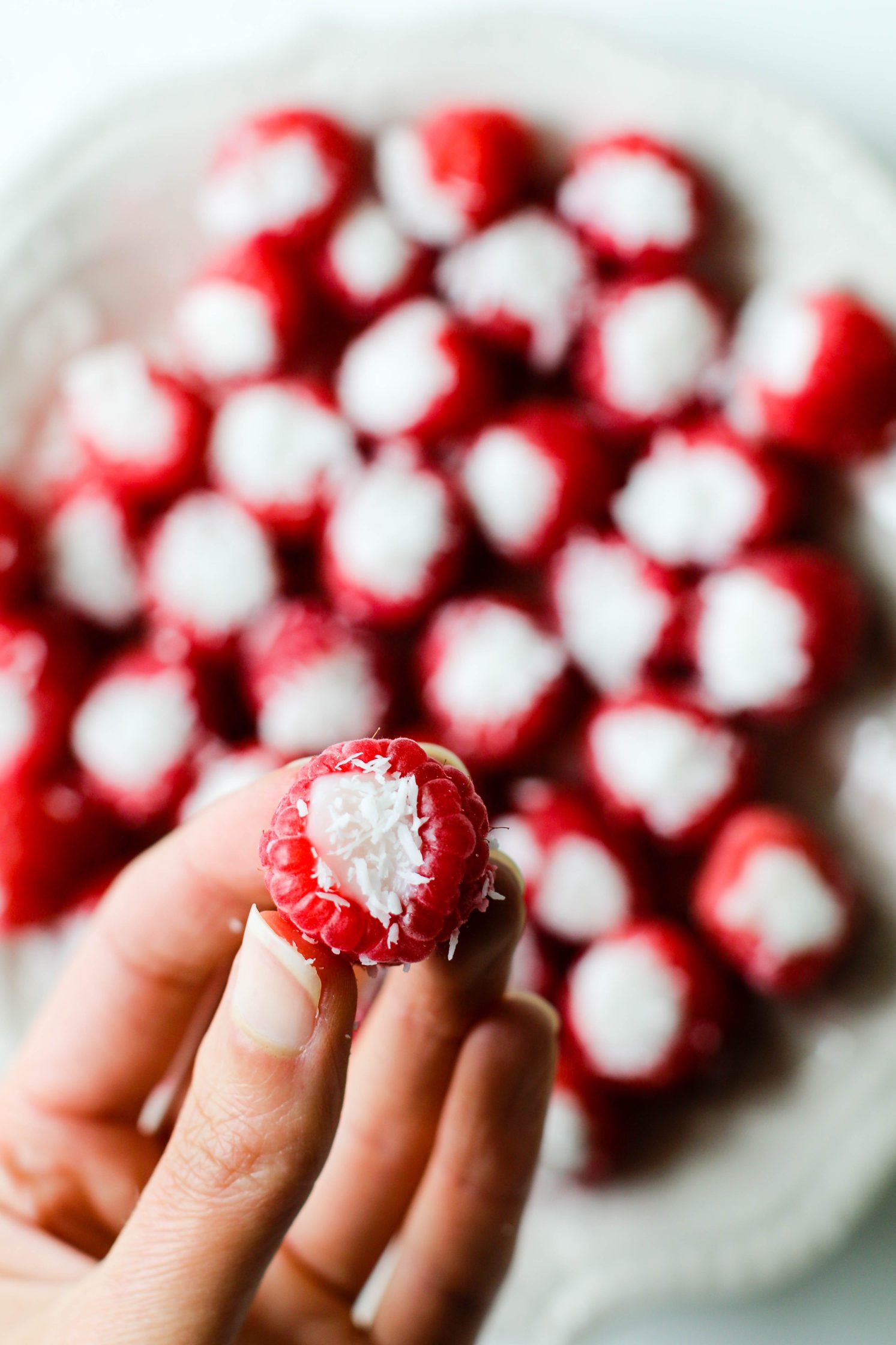Coconut Stuffed Raspberries served on plate with hand holding one up