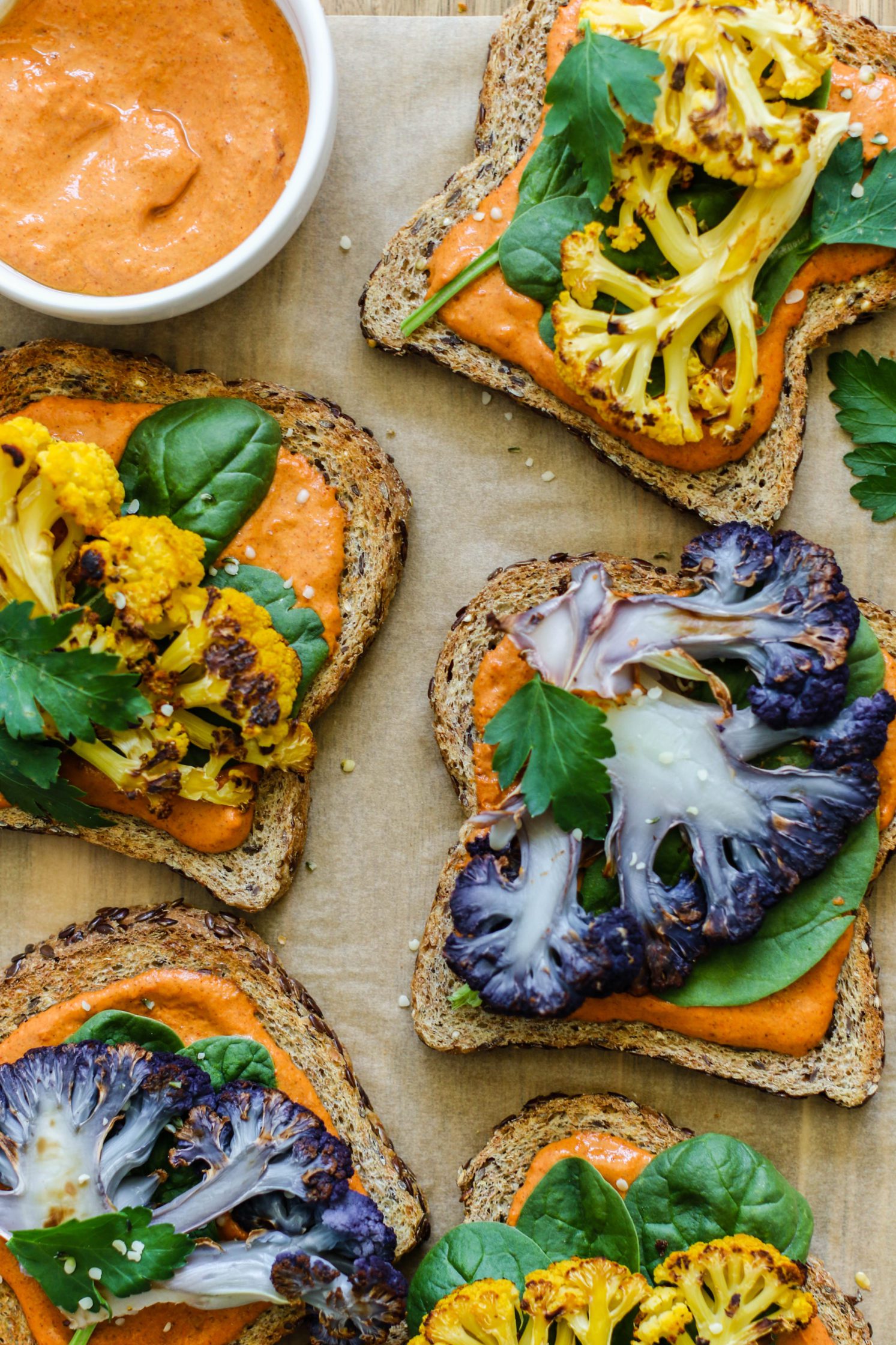 Romesco Roasted Cauliflower Toasts served on parchment paper with bowl of romesco sauce