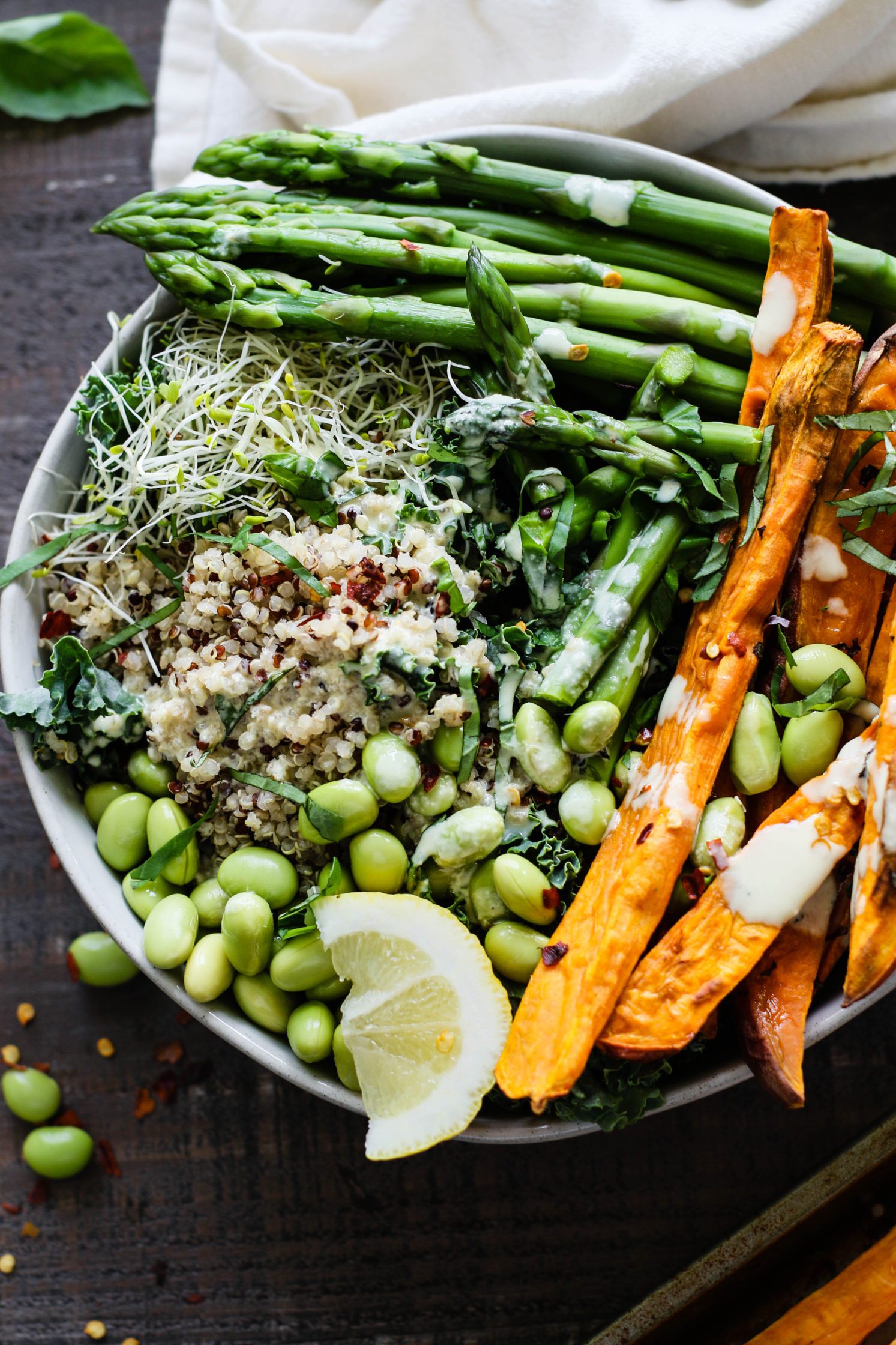 Lemon Basil Buddha Bowls served in bowls and drizzled with lemon tahini with jar of lemons and fresh basil and sweet potato fries on the side by Flora & Vino