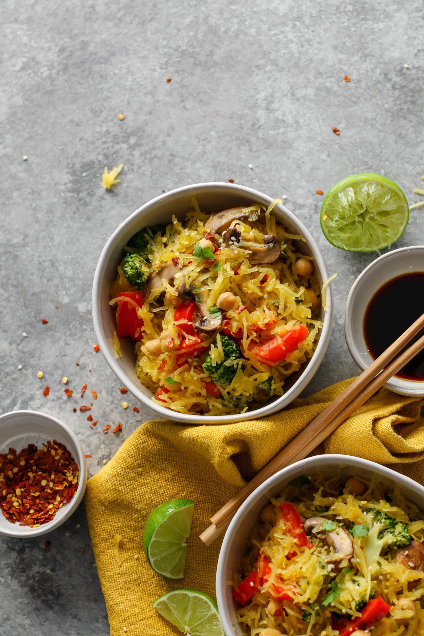 Spaghetti Squash Noodle Bowls overhead with chopsticks, limes, cilantro, sesame, red pepper flakes, and soy sauce by Flora & Vino 