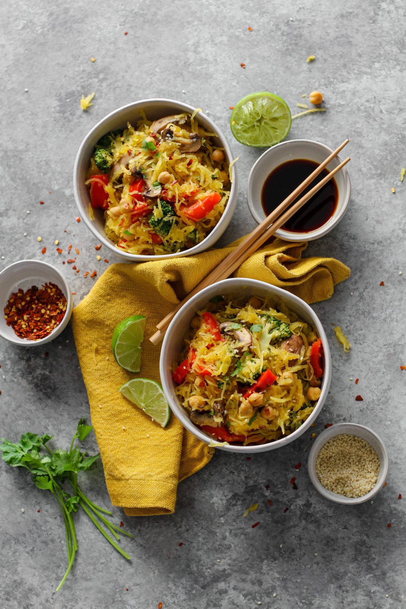 Spaghetti Squash Noodle Bowls overhead with chopsticks, limes, cilantro, sesame, red pepper flakes, and soy sauce by Flora & Vino 
