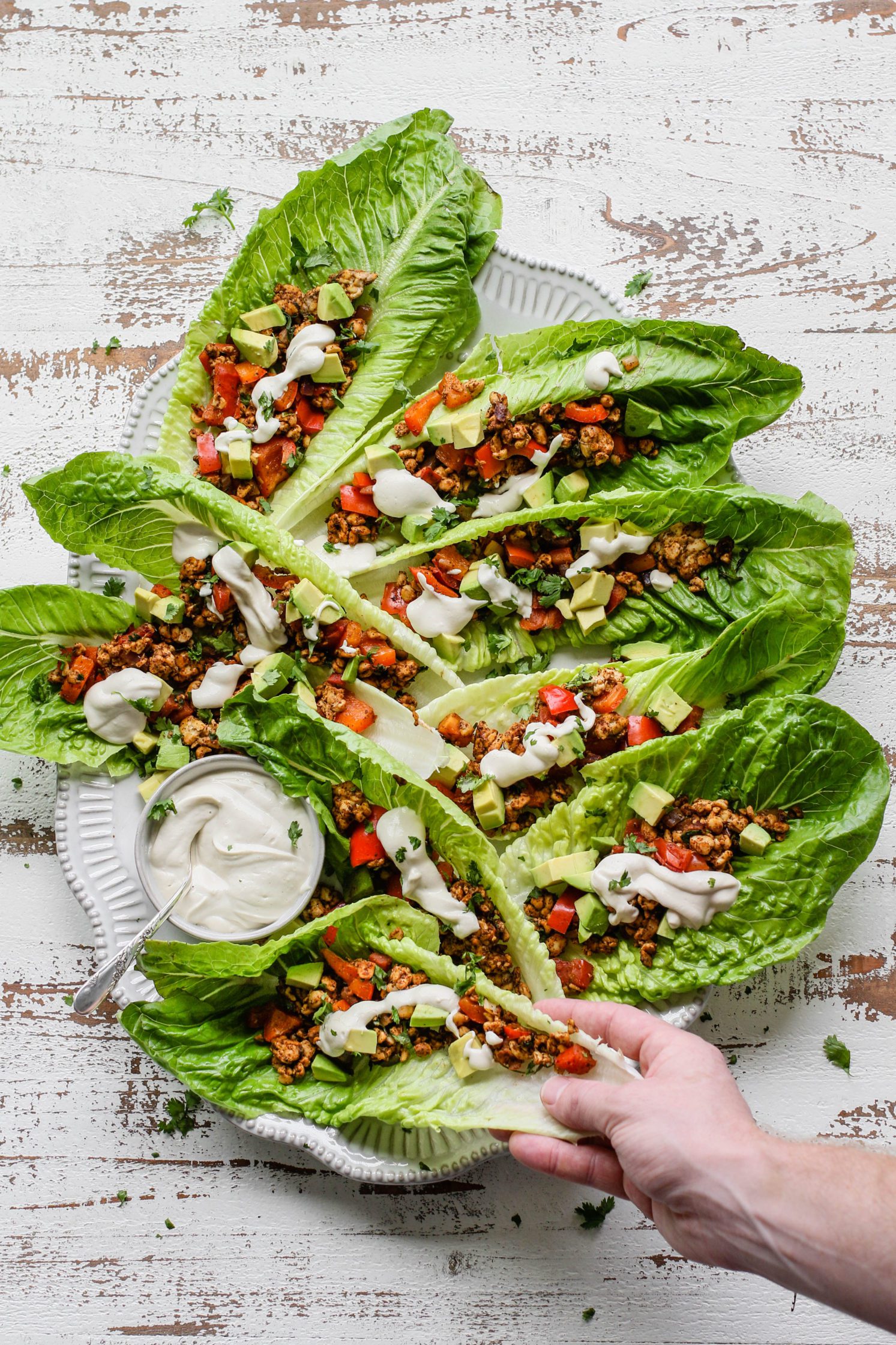 hand reaching for Romaine Tempeh Tacos served on plate with Cashew Sour Cream and spoon