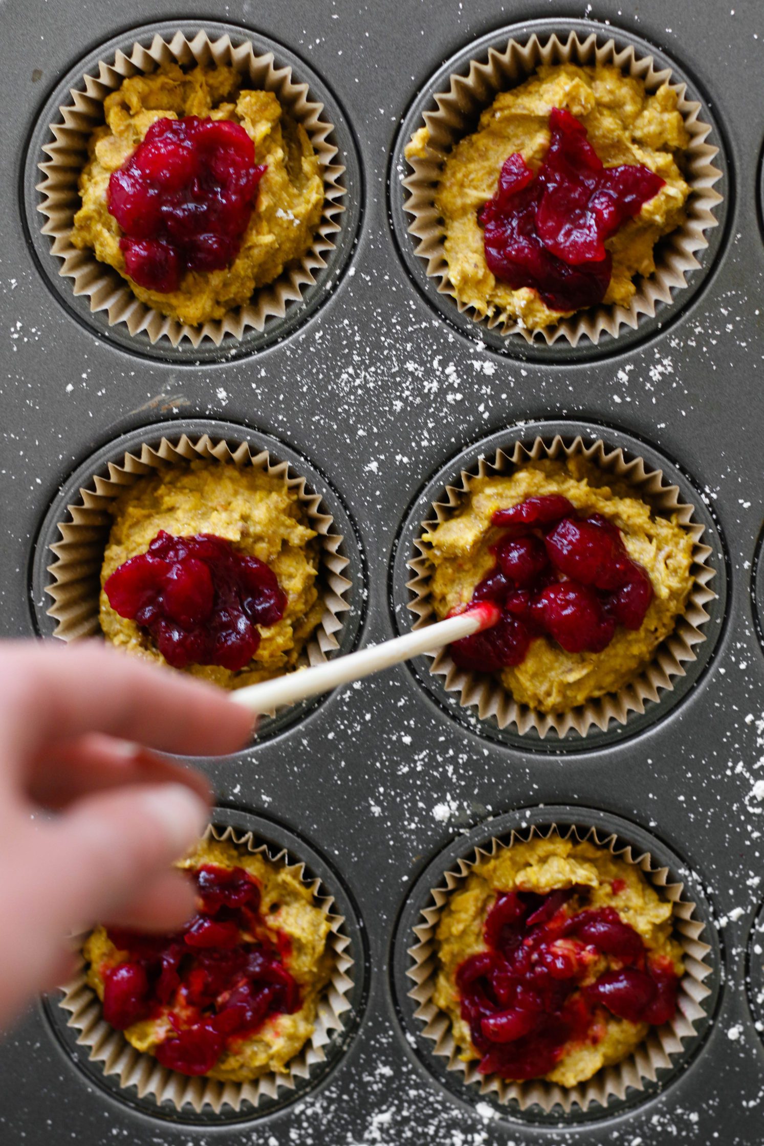 kabocha squash muffin batter with hand swirling cranberry sauce on top by Flora & Vino