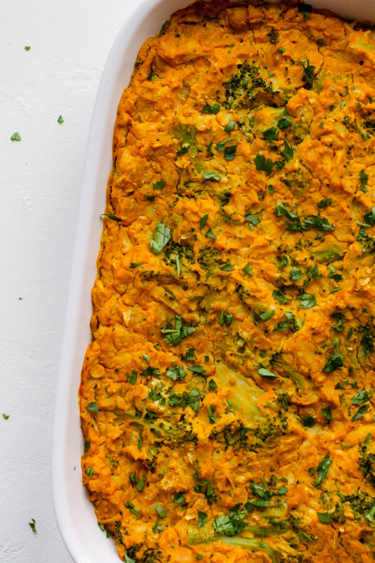 “Cheezy” Chickpea & Broccoli Casserole in casserole dish with parsley on top by Flora & Vino