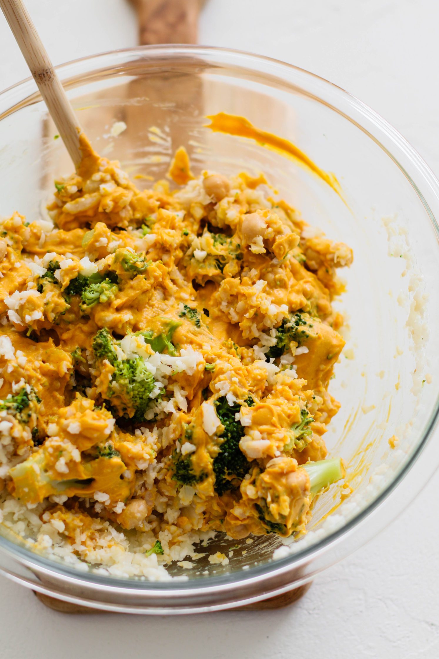 “Cheezy” Chickpea & Broccoli Casserole mixture in bowl with wooden spoon by Flora & Vino