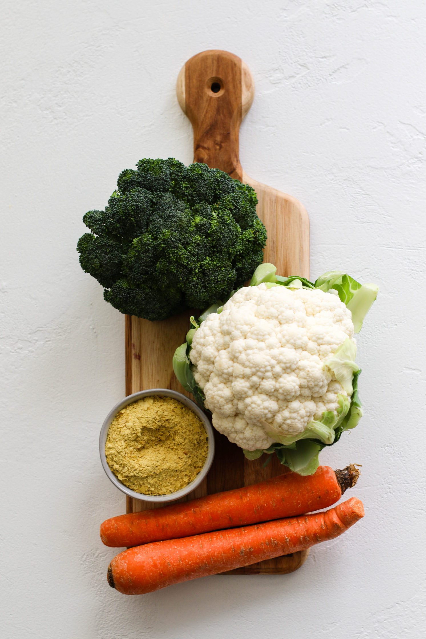 broccoli, cauliflower, carrots, and nutritional yeast on cutting board by Flora & Vino