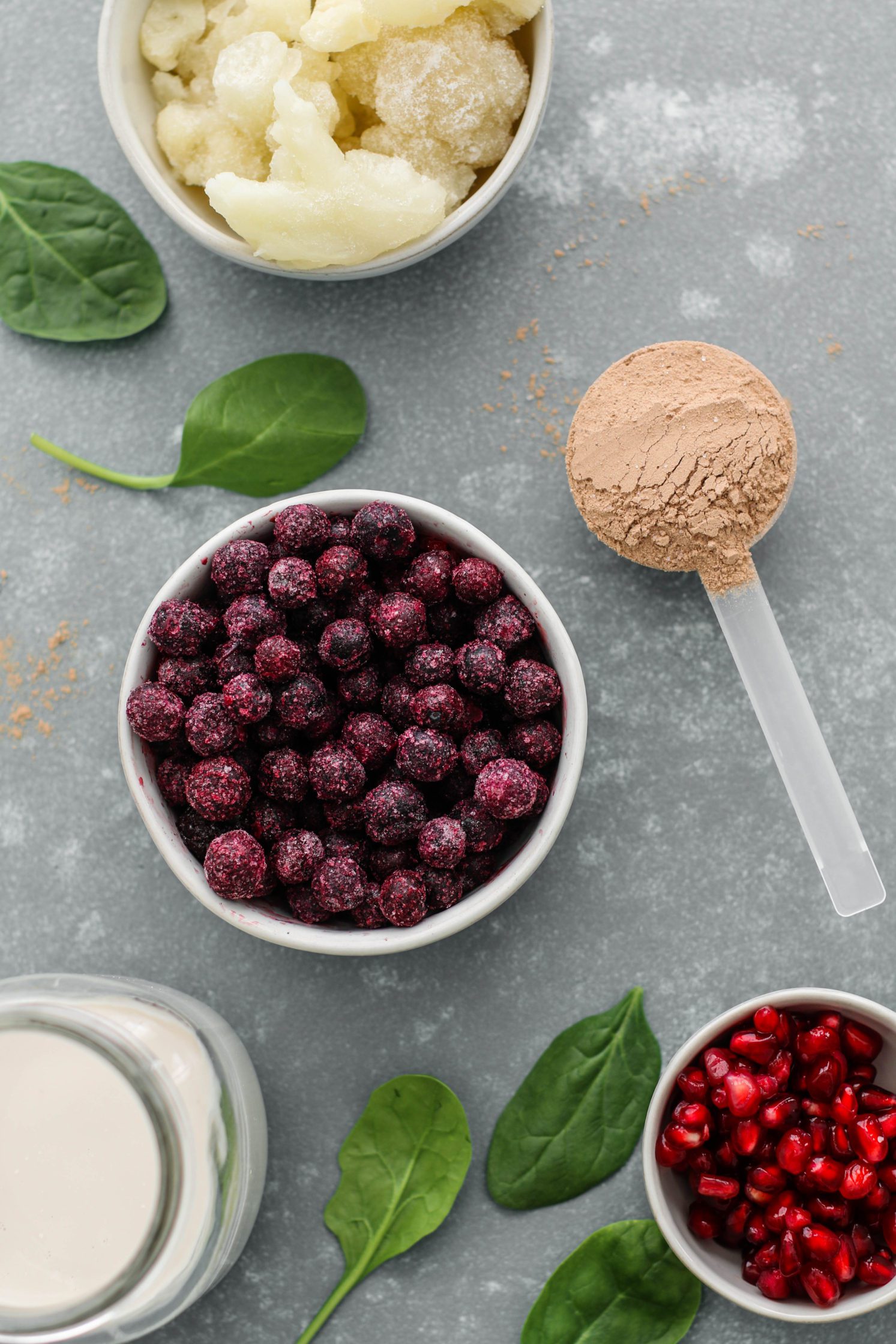 frozen blueberries, frozen cauliflower, chocolate protein powder, pomegranate, and spinach on wooden board by Flora & Vino