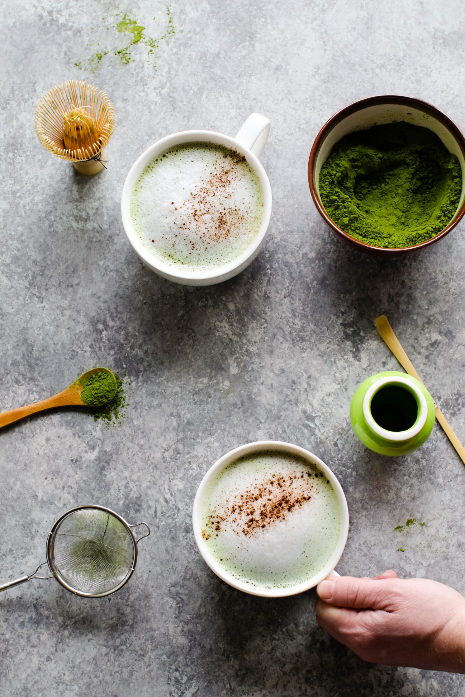 Cinnamon Almond Matcha Latte served in mugs with hand grabbing one by Flora & Vino