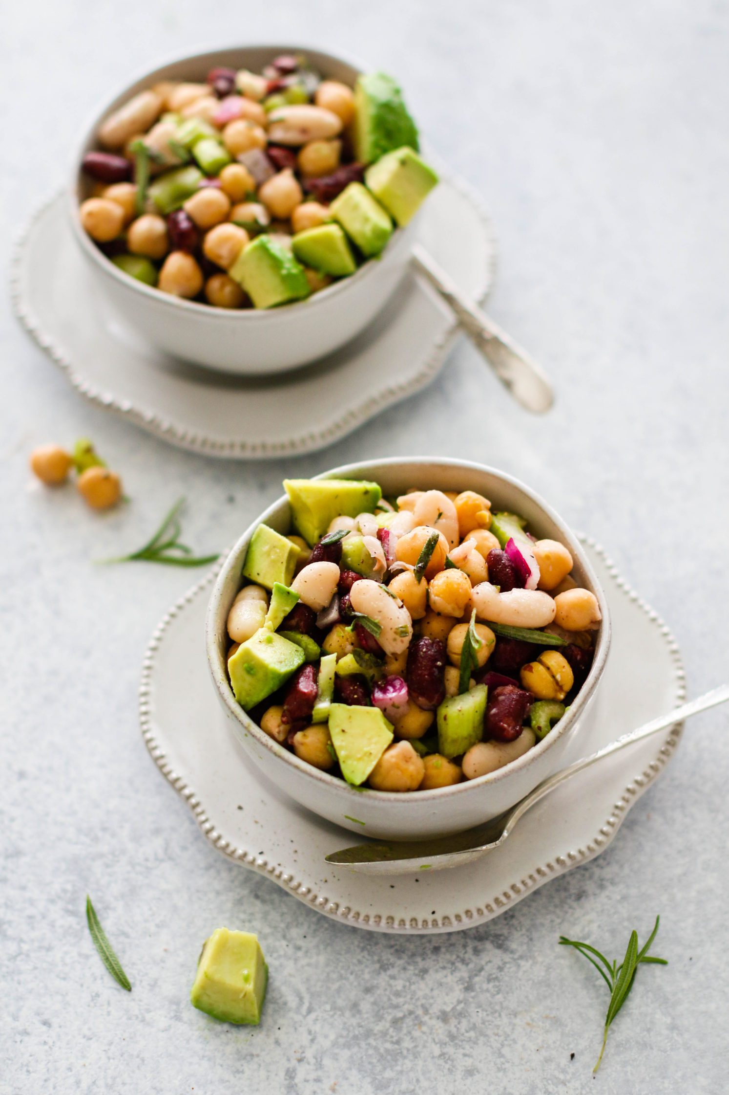 Rosemary Three Bean Salad served in white bowls with avocado and a spoon