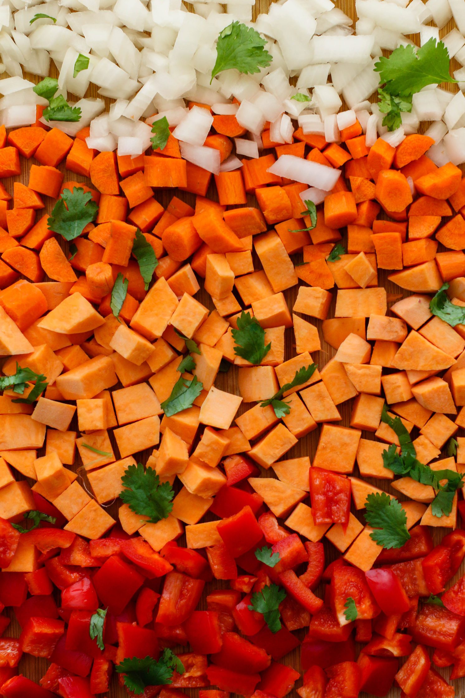 chopped sweet potatoes, onions, and bell pepper on cutting board with cilantro by Flora & Vino