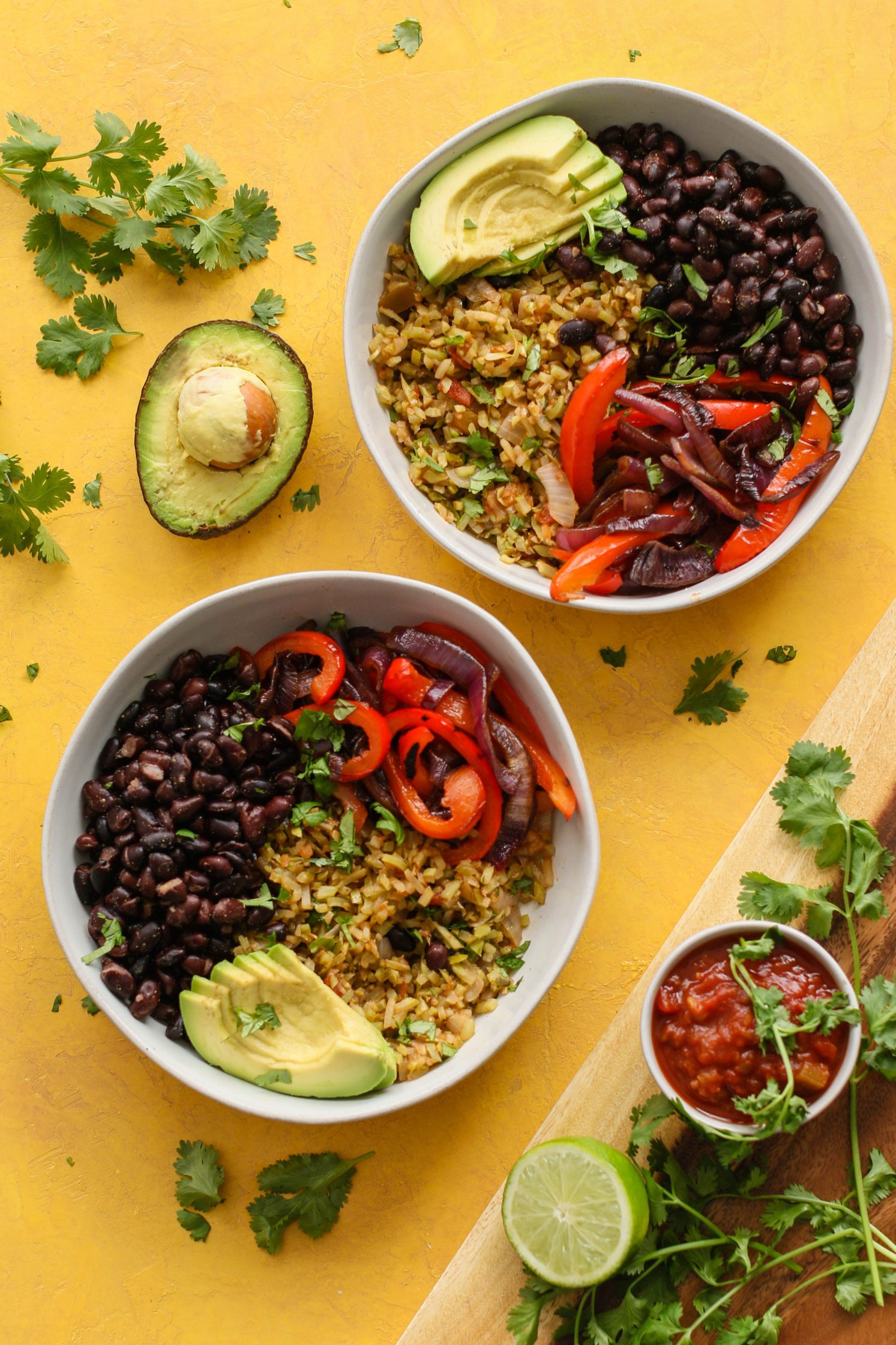 Broccoli Lime Rice & Black Bean Burrito Bowls in bowls topped with avocado, cilantro, and salsa on yellow board by Flora & Vino 