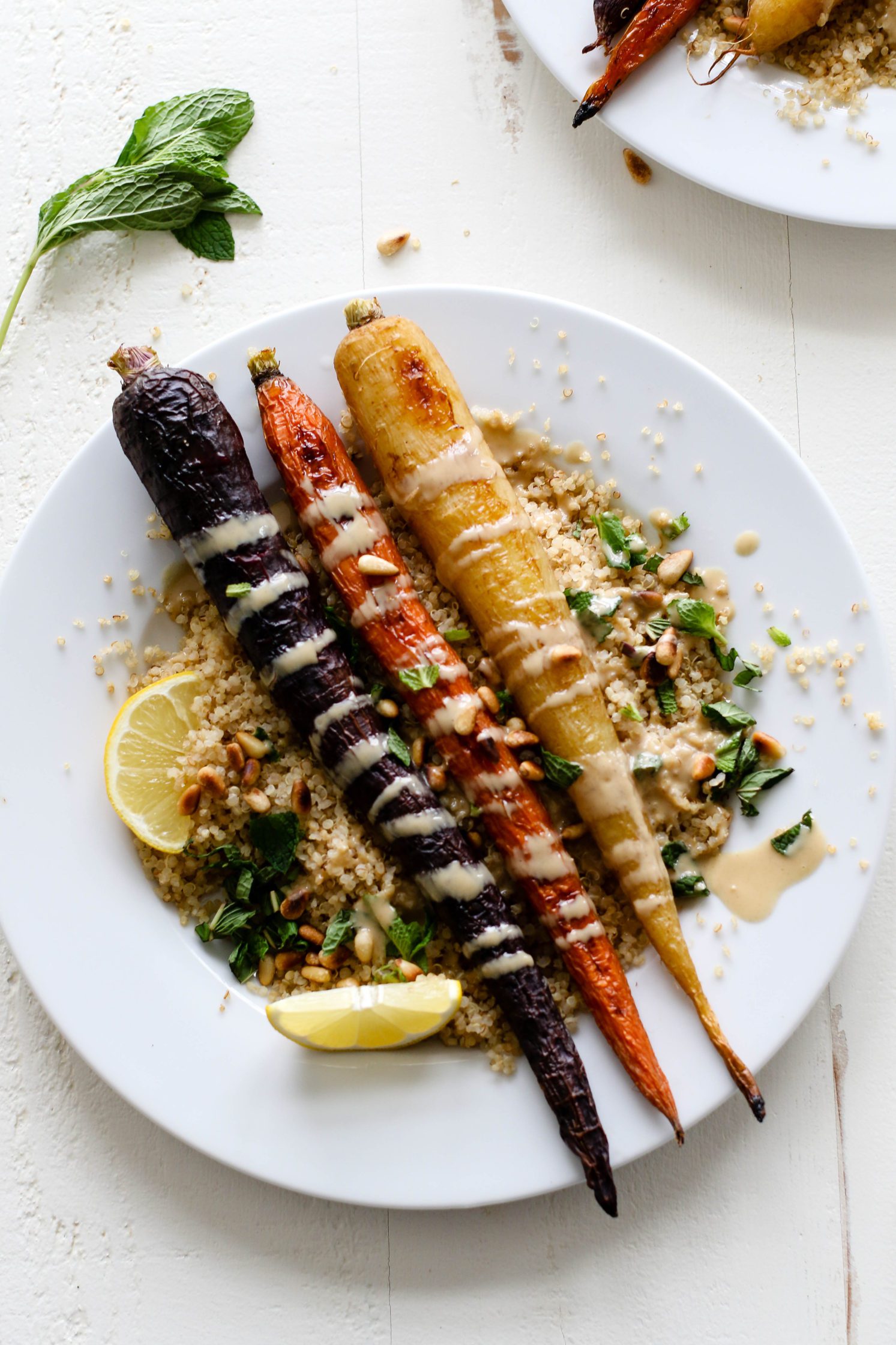 Rainbow Roasted Carrots served on plates over quinoa with fresh lemon, shredded mint, toasted pine nuts, and drizzle of tahini