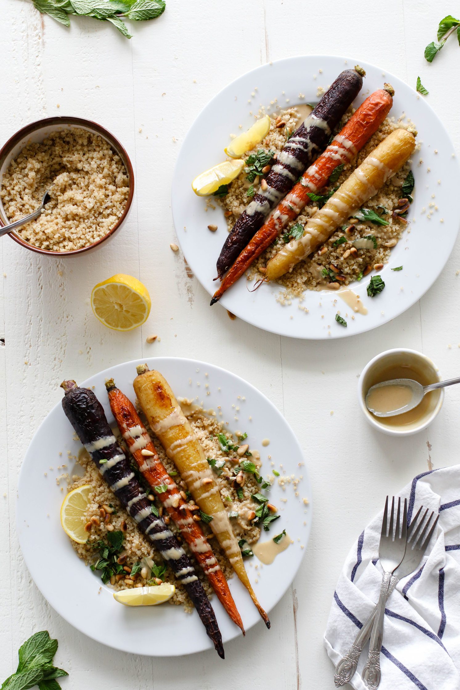 Rainbow Roasted Carrots served on plates over quinoa with fresh lemon, shredded mint, toasted pine nuts, and drizzle of tahini