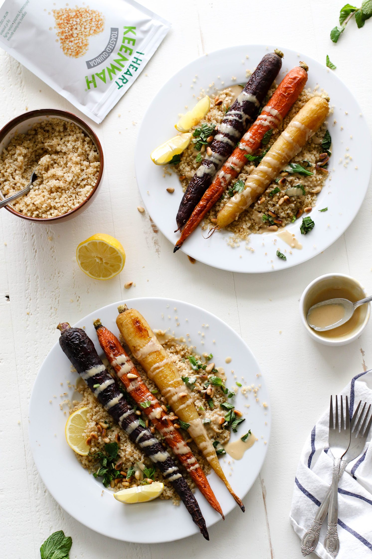 Rainbow Roasted Carrots served on plates over quinoa with fresh lemon, shredded mint, toasted pine nuts, and drizzle of tahini