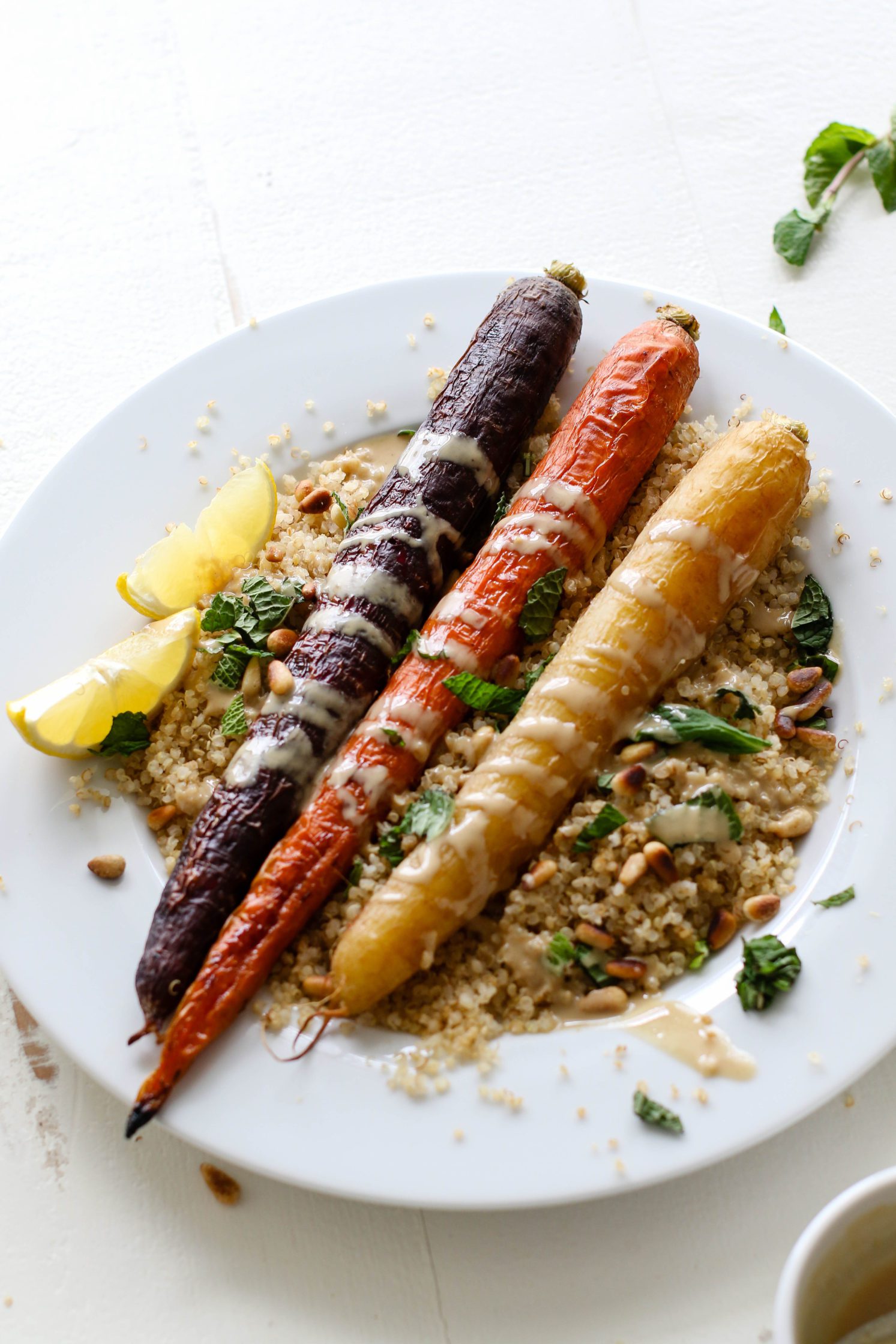 Rainbow Roasted Carrots served on plate over quinoa with fresh lemon, shredded mint, toasted pine nuts, and drizzle of tahini