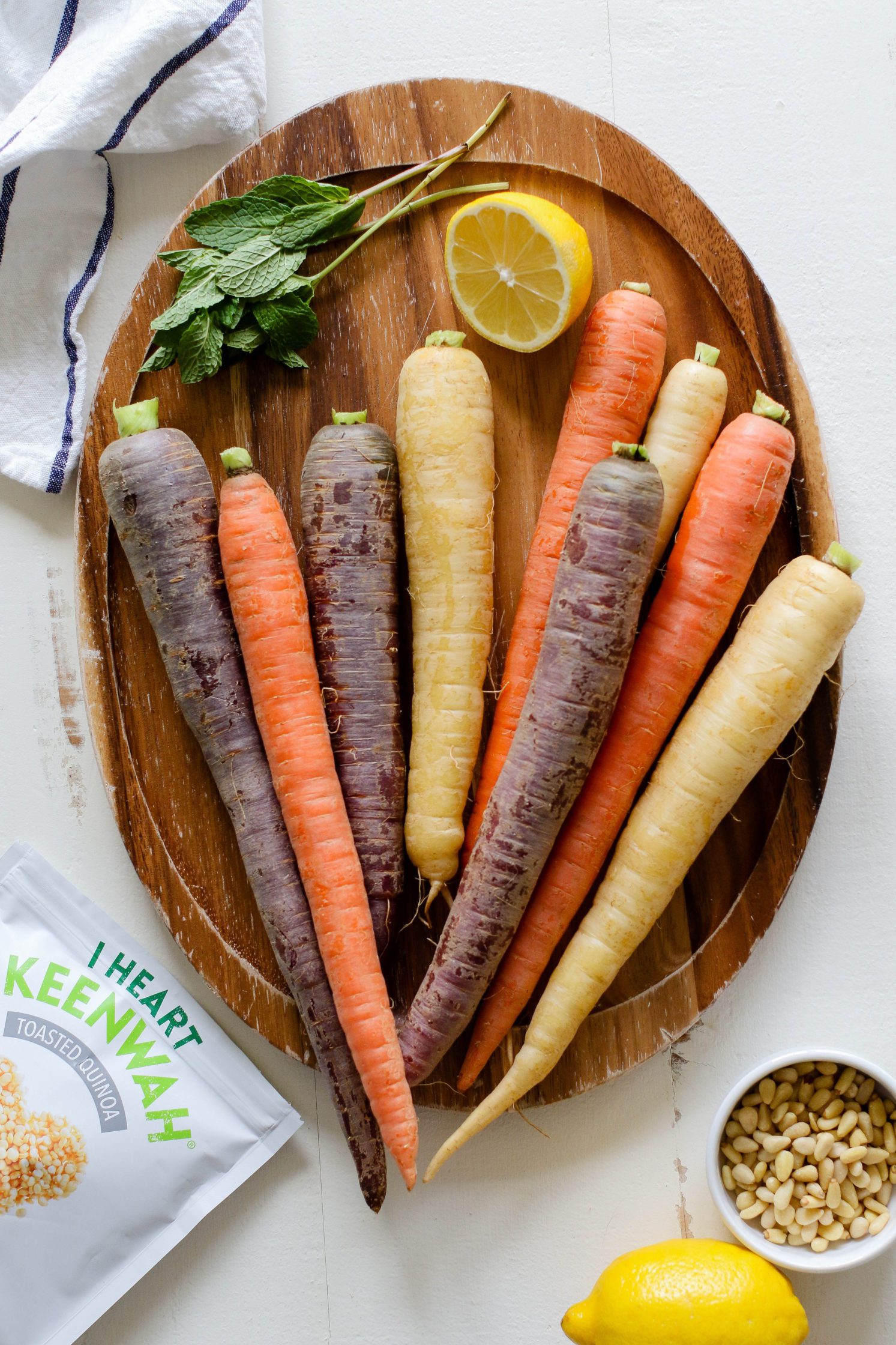 rainbow carrots on wooden board with lemon and fresh mint with pine nuts and white and blue striped towel on the side