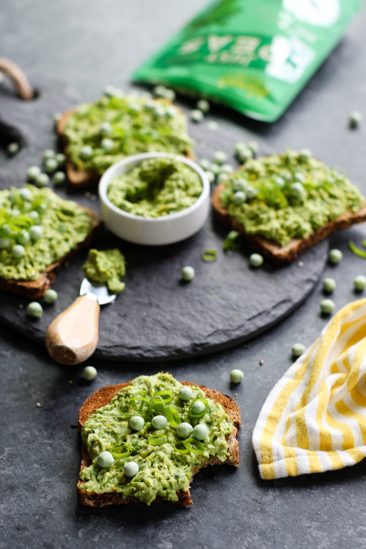 Lemon-y Smashed Pea Toasts on serving platter with bite out of one toast