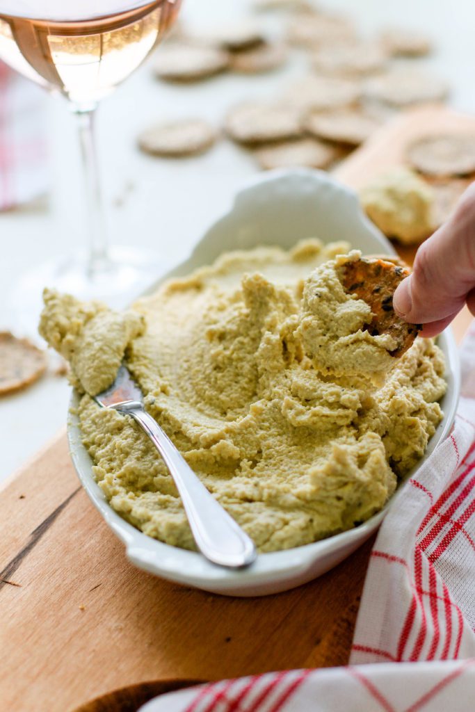 hand dipping cracker into raw cashew cheese by Flora & Vino