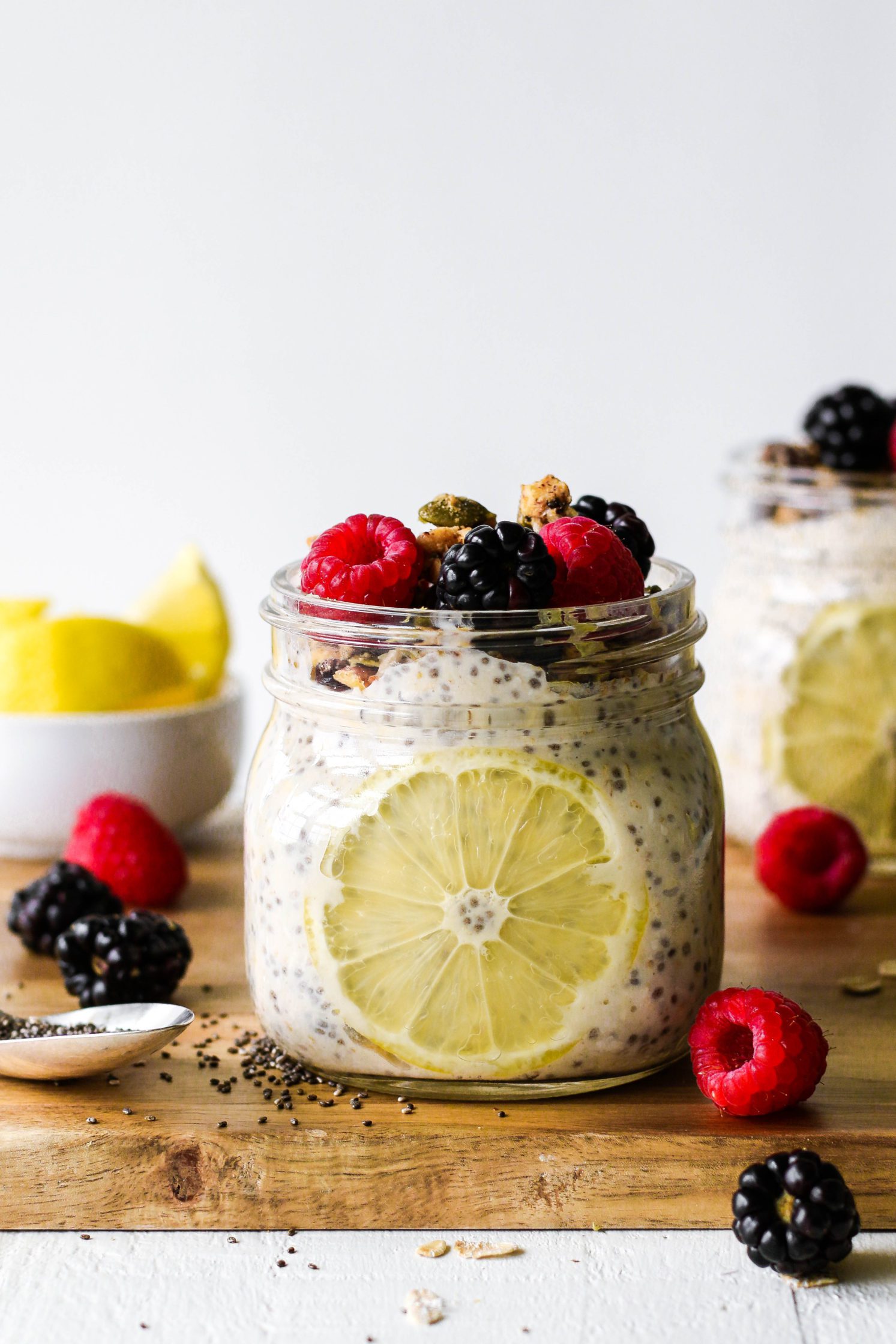 Lemon Berry Chia Overnight Oats served in mason jar on top of wooden board topped with fresh raspberries and blackberries by Flora & Vino