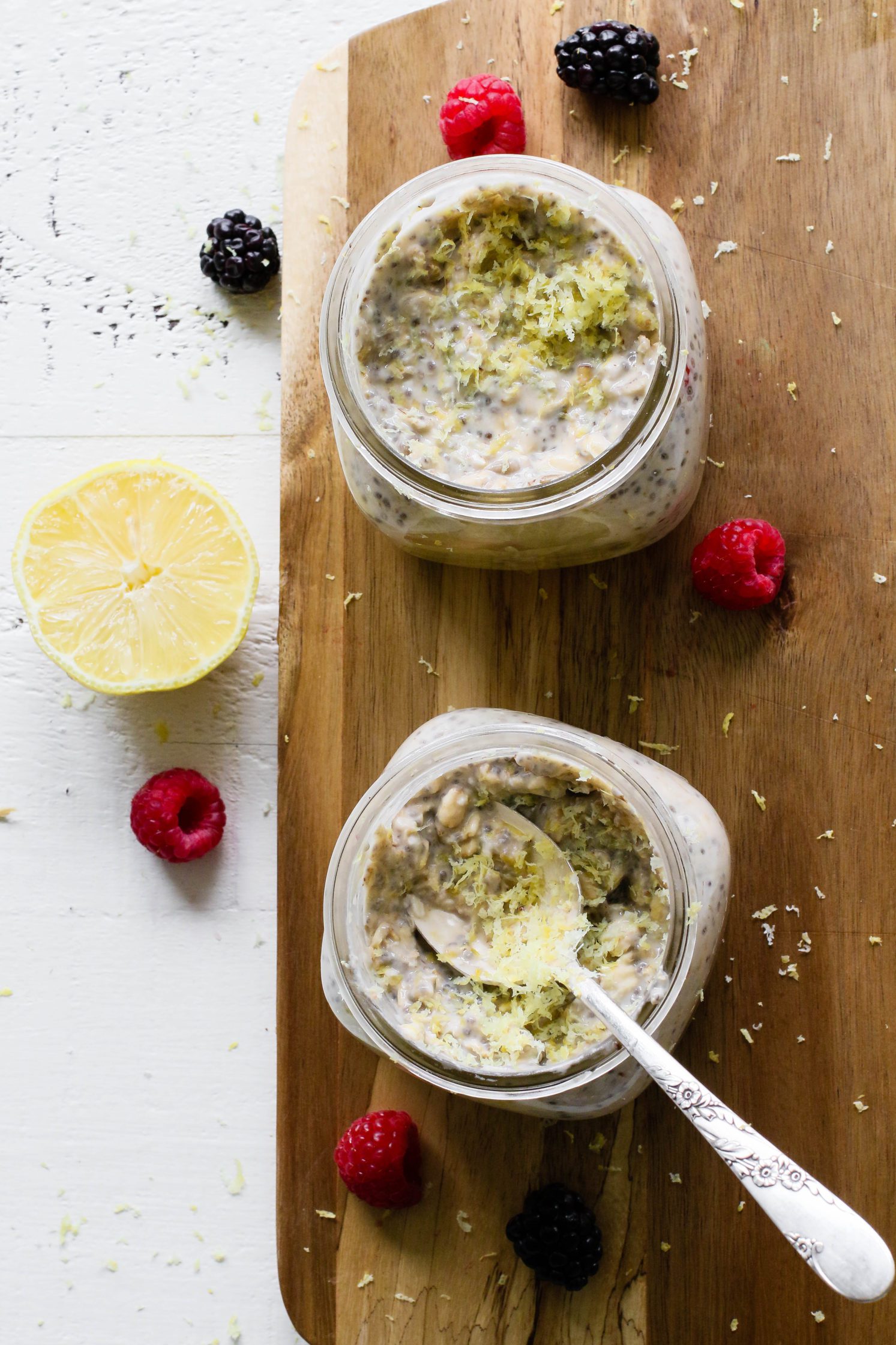 Lemon Berry Chia Overnight Oats mixed in mason jars on a wooden board with fresh berries and a spoon by Flora & Vino