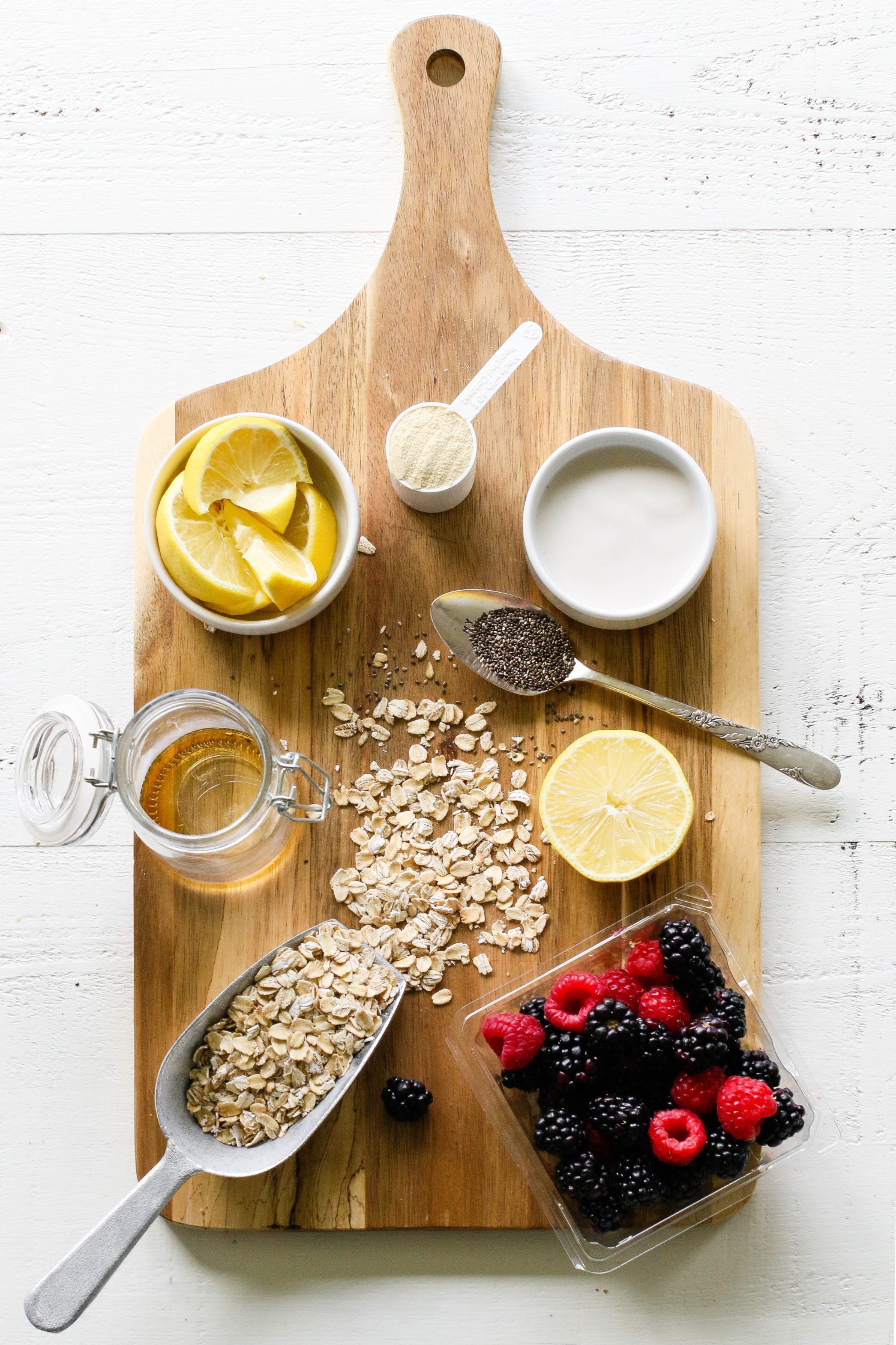 sliced lemons, vanilla protein powder, yogurt, oatmeal, maple syrup, and berries on wooden board by Flora & Vino