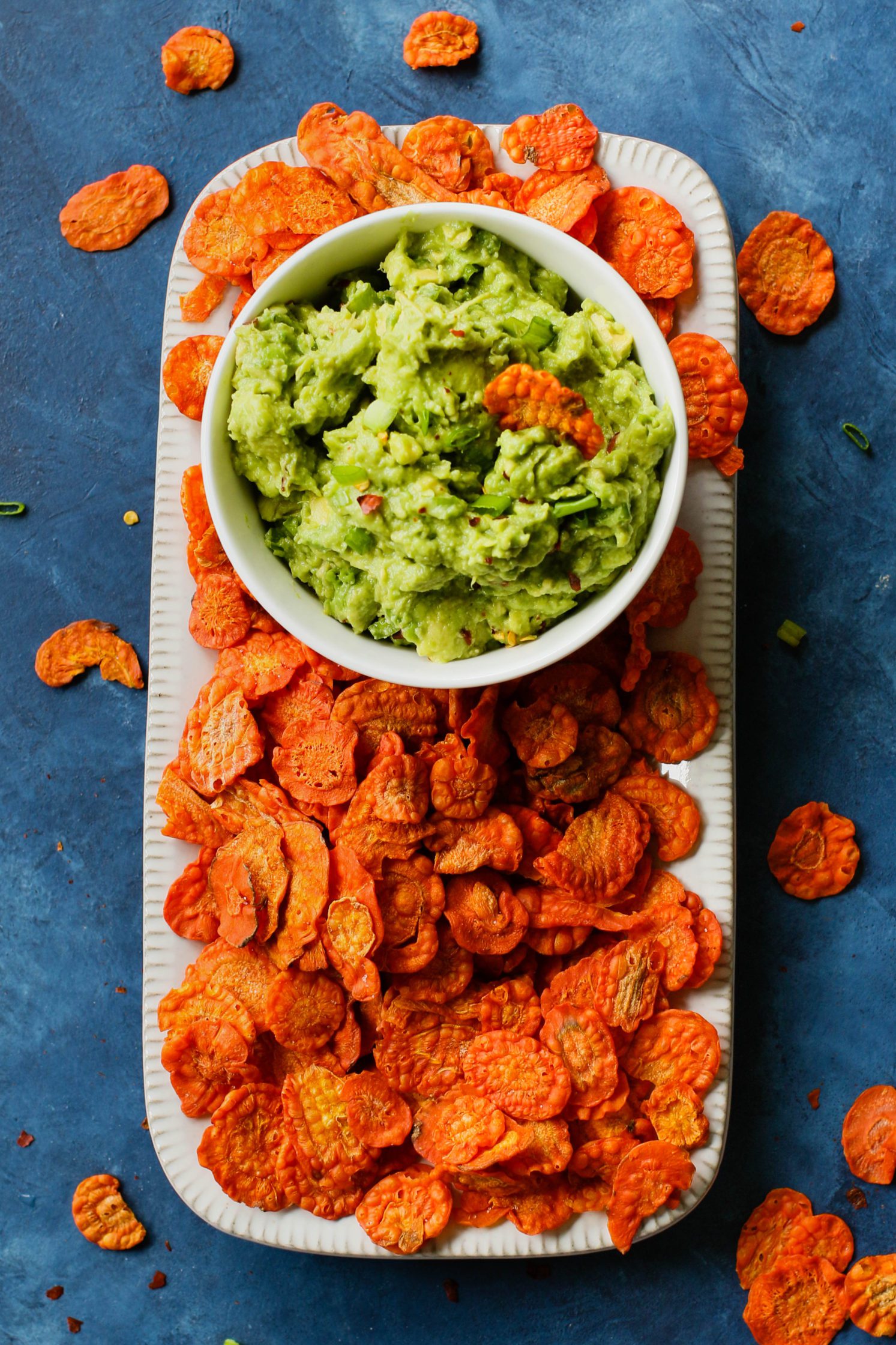 Perfect 5-Ingredient Guacamole served in a bowl with carrot chip dipped in by Flora & Vino