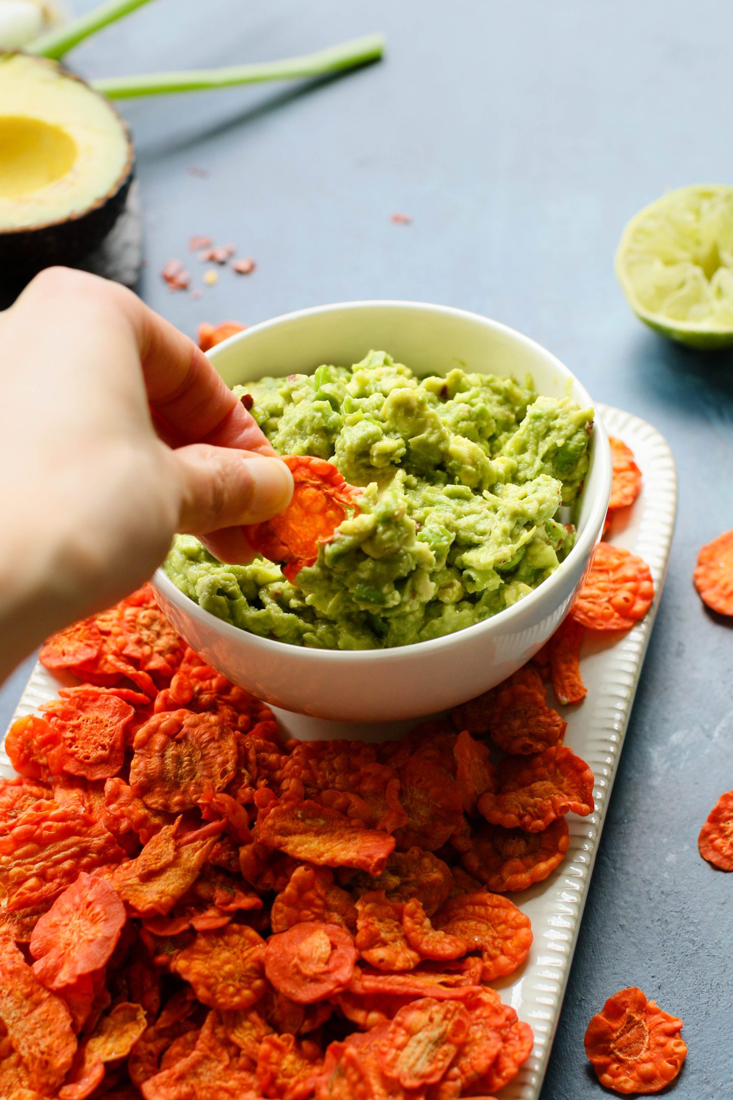 hand dipping carrot chip in Perfect 5-Ingredient Guacamole by Flora & Vino