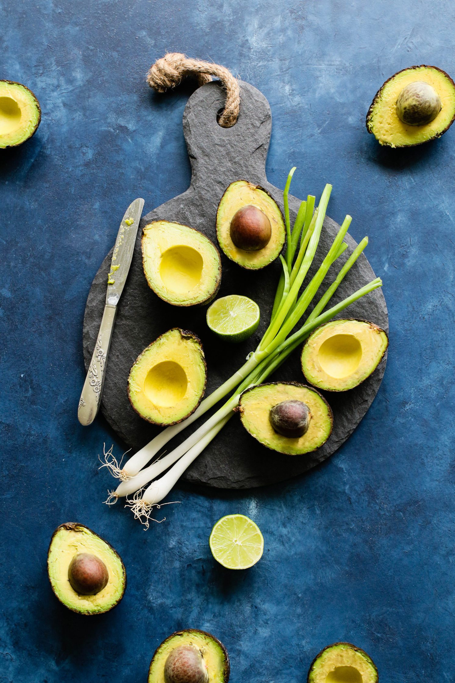 avocados cut in half with lime and green onion on serving board by Flora & Vino