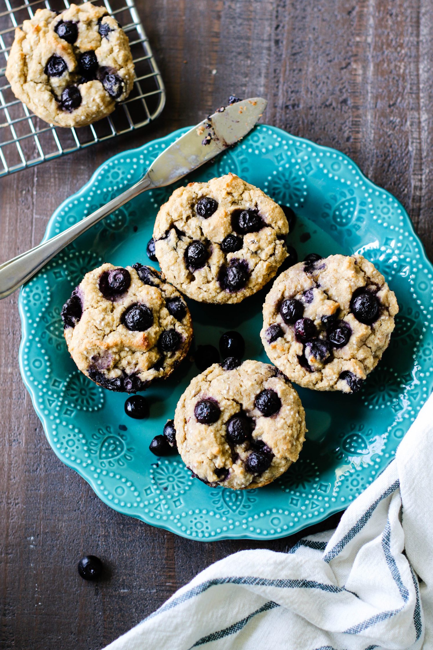 The Best Vegan & Gluten Free Blueberry Muffins served on blue plate with a knife on wooden board