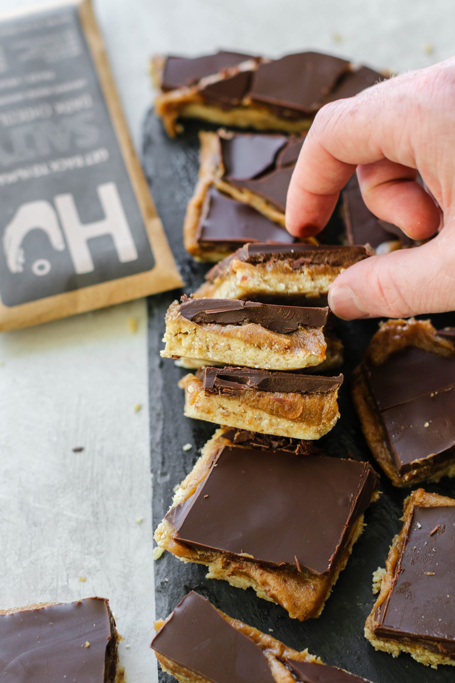 Vegan Chocolate Nougat Bars sliced on cutting board with hand reaching for one by Flora & Vino