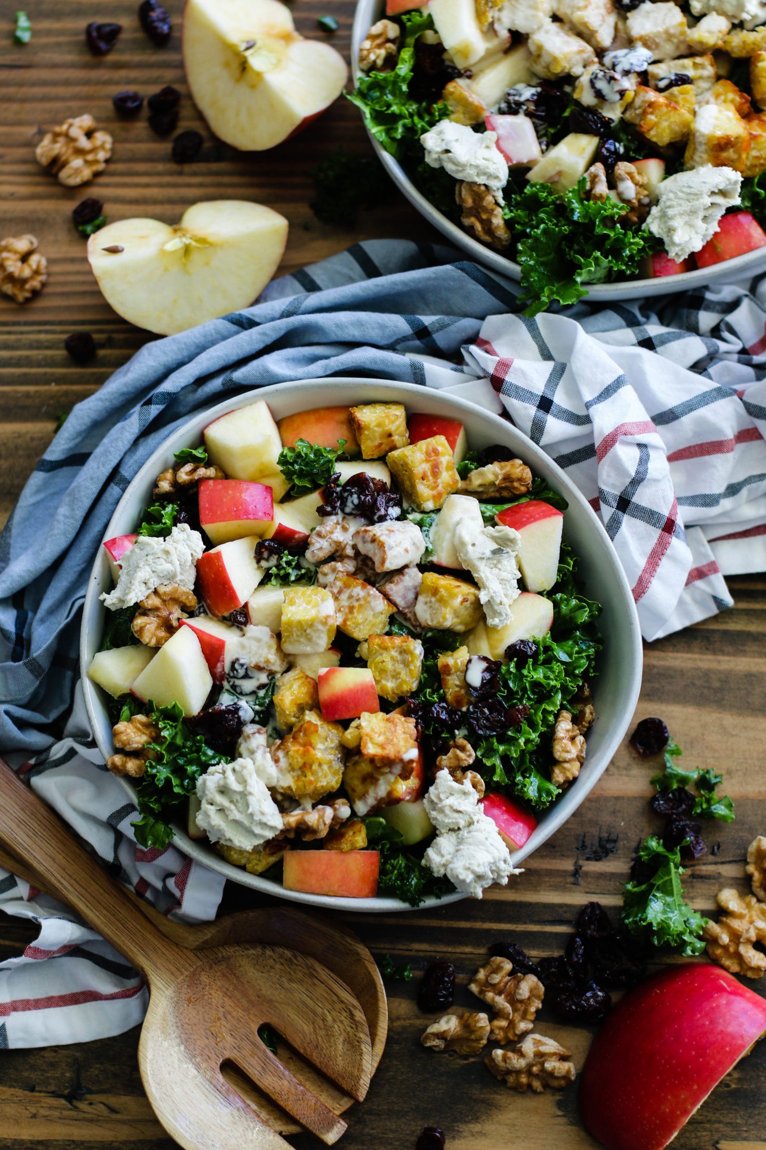 Cran-Apple Tempeh Kale Salad served in bowls with apples and walnuts scattered by Flora & Vino