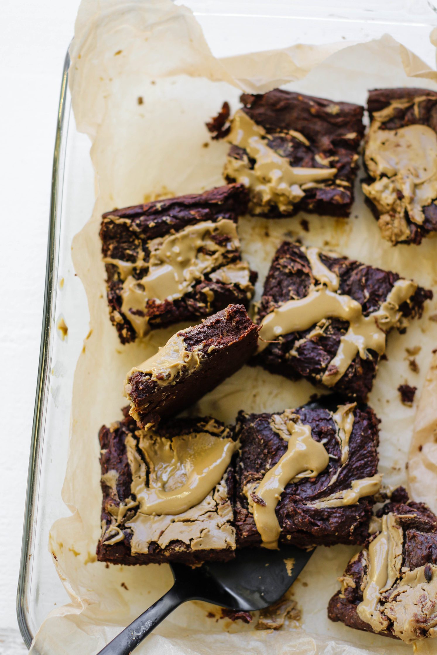 Avocado SunButter Swirl Brownies cut into squares in parchment lined baking dish 