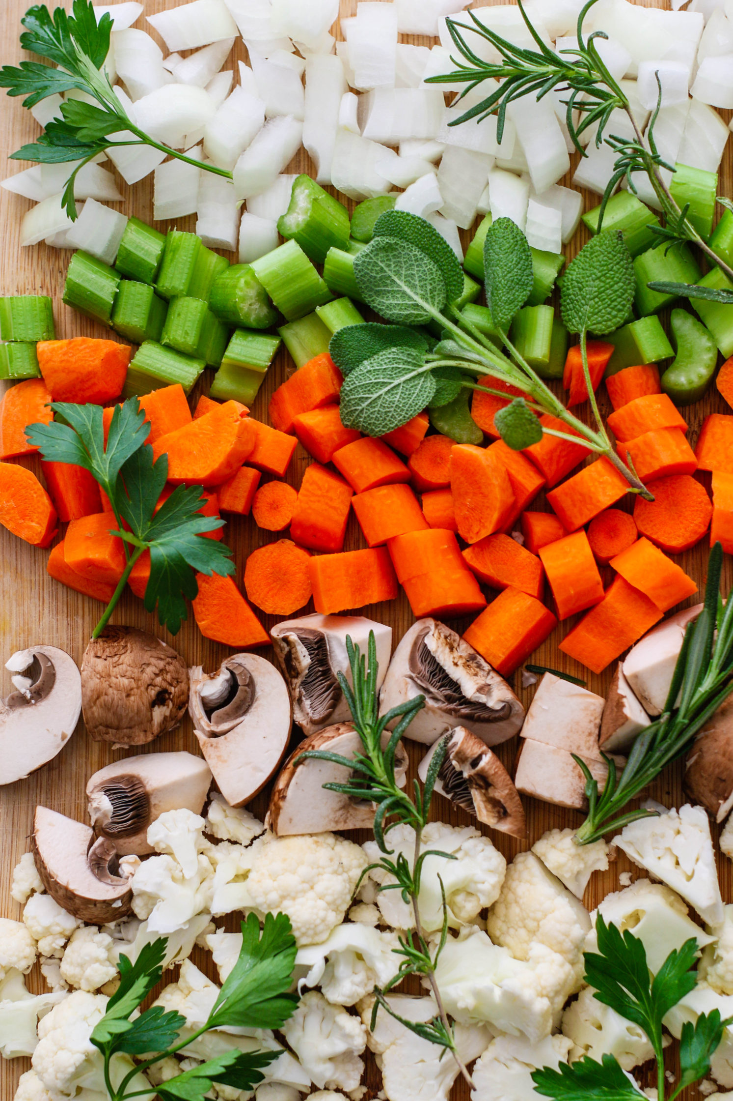chopped onion, celery, carrots, mushrooms, and cauliflower on cutting board by Flora & Vino