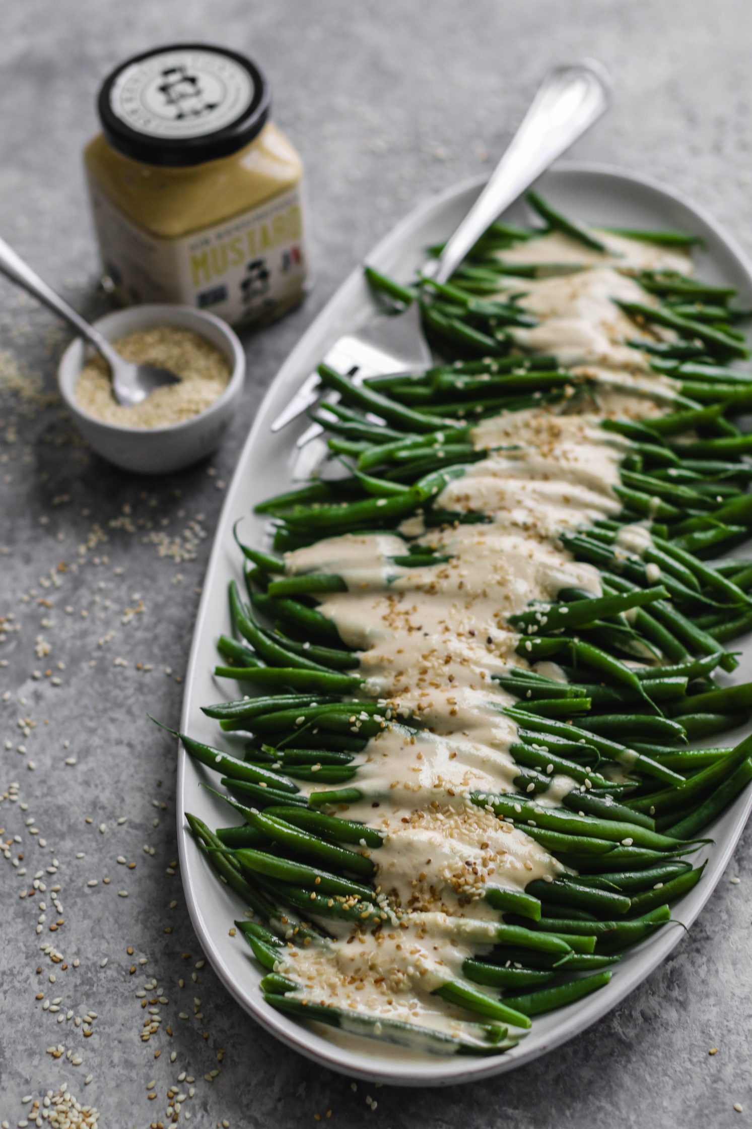 Dijon Tahini Green Beans served on platter with fork and sesame seeds by Flora & vino