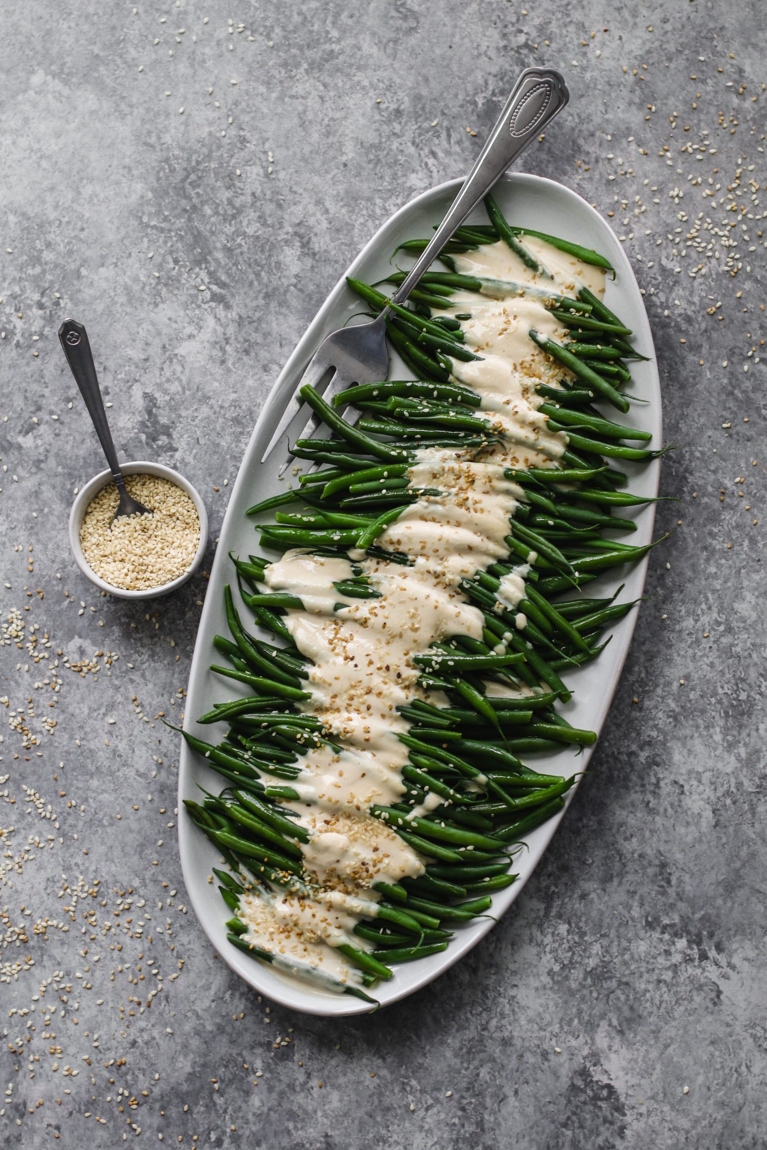 Dijon Tahini Green Beans served on platter with fork and sesame seeds by Flora & Vino