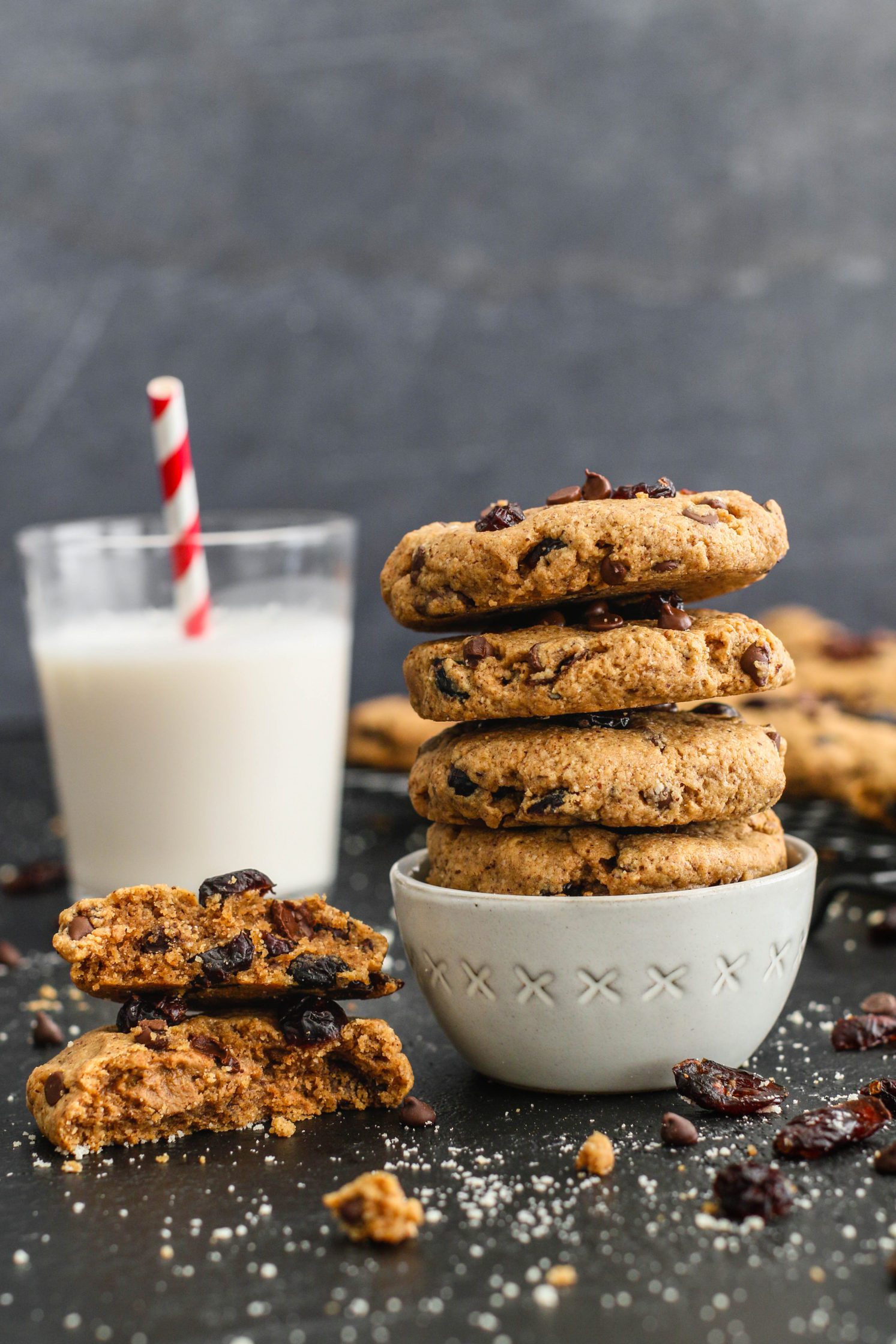Cranberry Chocolate Chip Cookies stacked in a bowl with milk glass behind them by Flora & Vino
