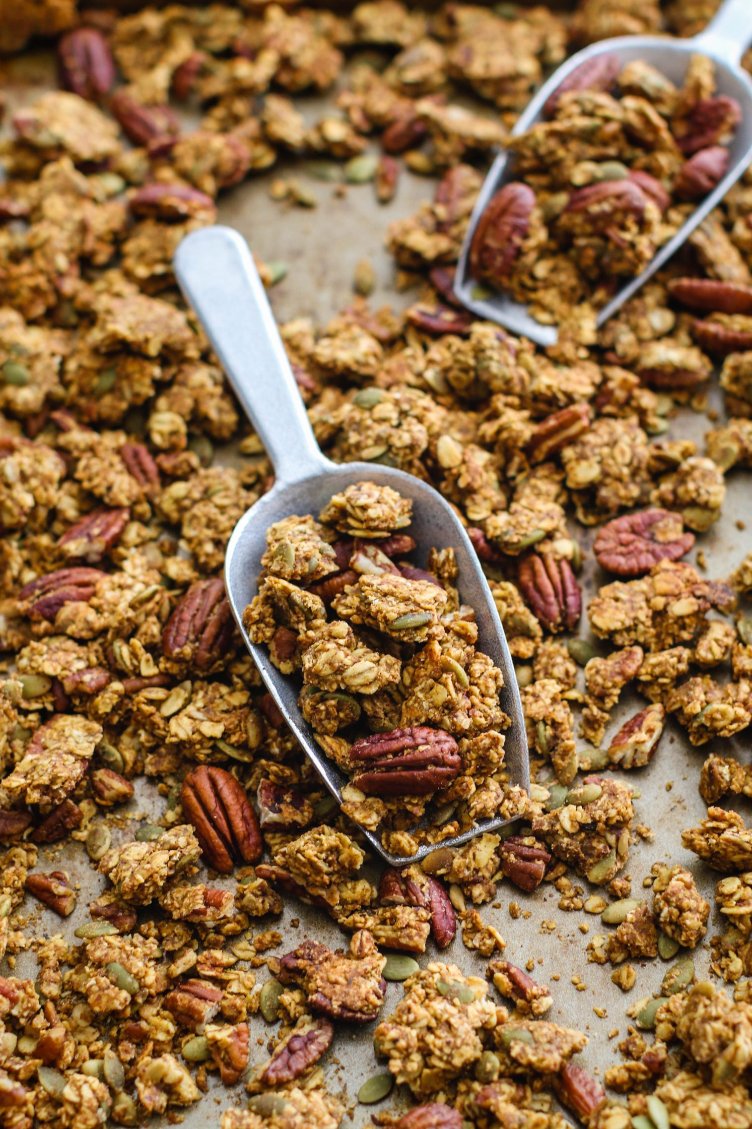 Pumpkin Spice Pecan Granola on baking sheet with 2 scoops by Flora & Vino