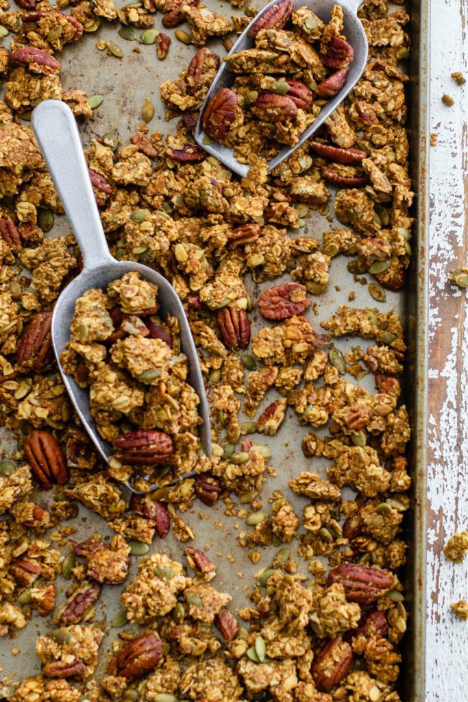 Pumpkin Spice Pecan Granola baked on parchment lined baking sheet with 2 scoops by Flora & Vino
