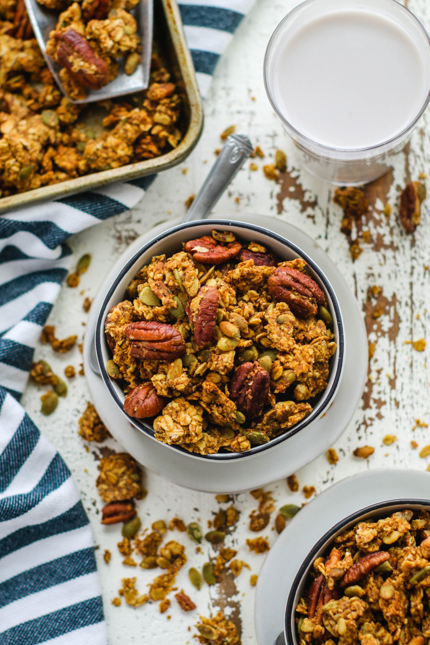 Pumpkin Spice Pecan Granola served in a bowl with a spoon and glass of almond milk by Flora & Vino